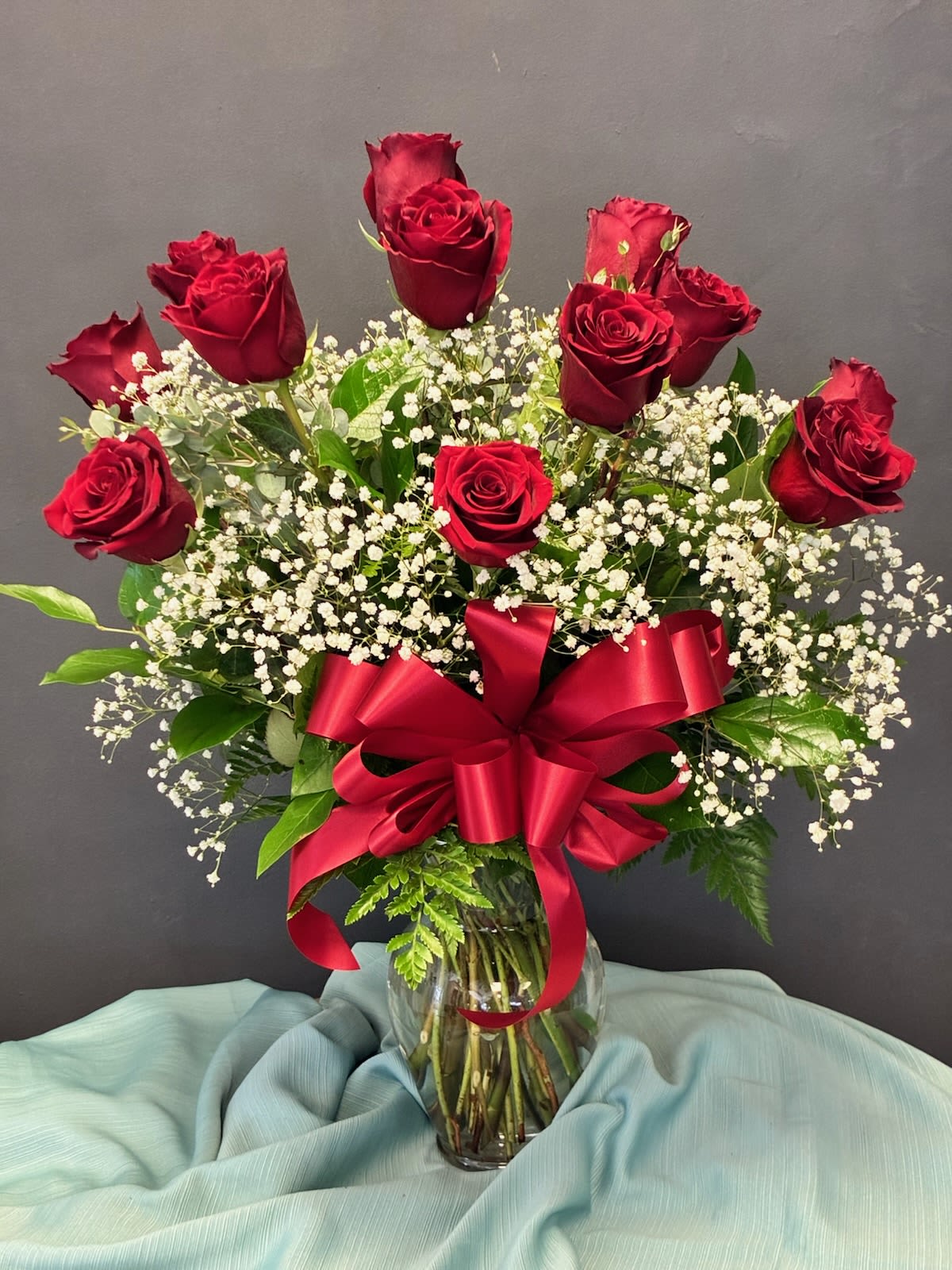 Red roses and baby's breath in a glass vase with a red ribbon