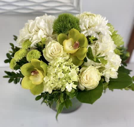 Compact arrangement of green orchids, white roses, hydrangeas, and mums in a round vase