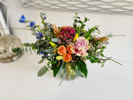 Mixed bouquet with orange roses, pink blooms, and blue flowers in a glass vase
