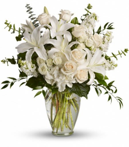 Tall arrangement of white lilies and roses in a clear glass vase