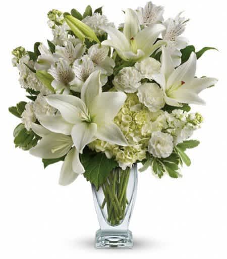 White lilies and mixed white flowers in a clear glass vase