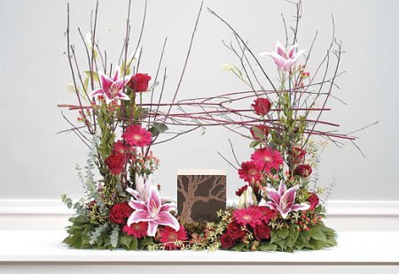 Tall floral arrangement with pink lilies and red flowers around a framed card