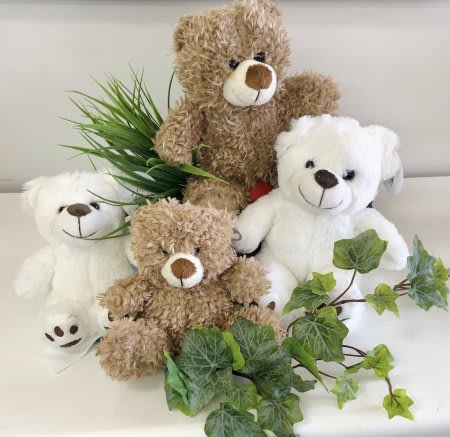 Three teddy bears with faux greenery on a white surface