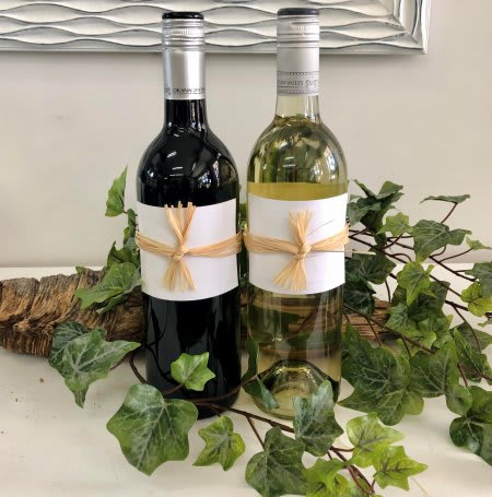Two wine bottles wrapped with raffia and surrounded by ivy