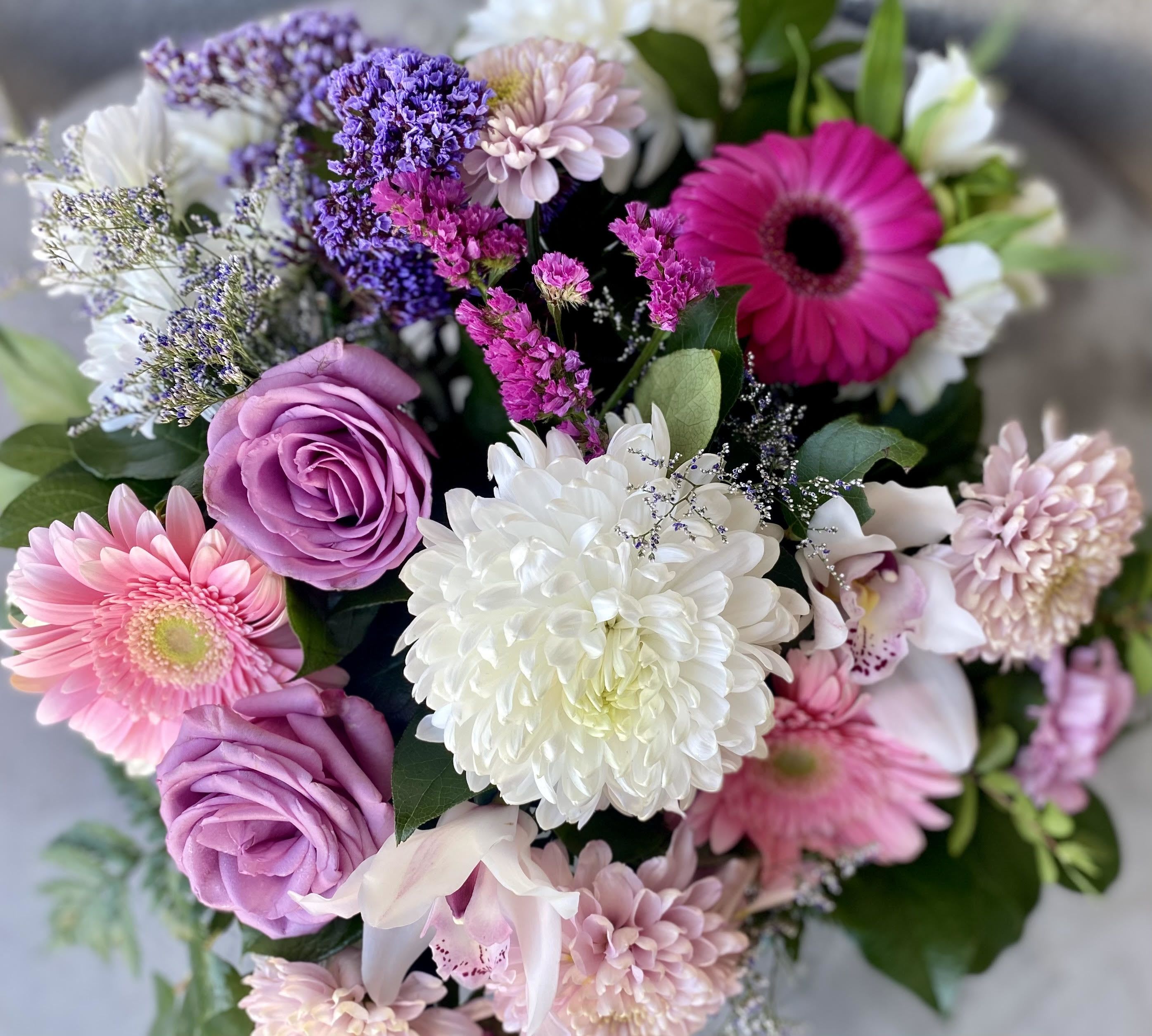 Mixed bouquet of pink gerbera daisies, lavender roses, white mums, and purple filler flowers.