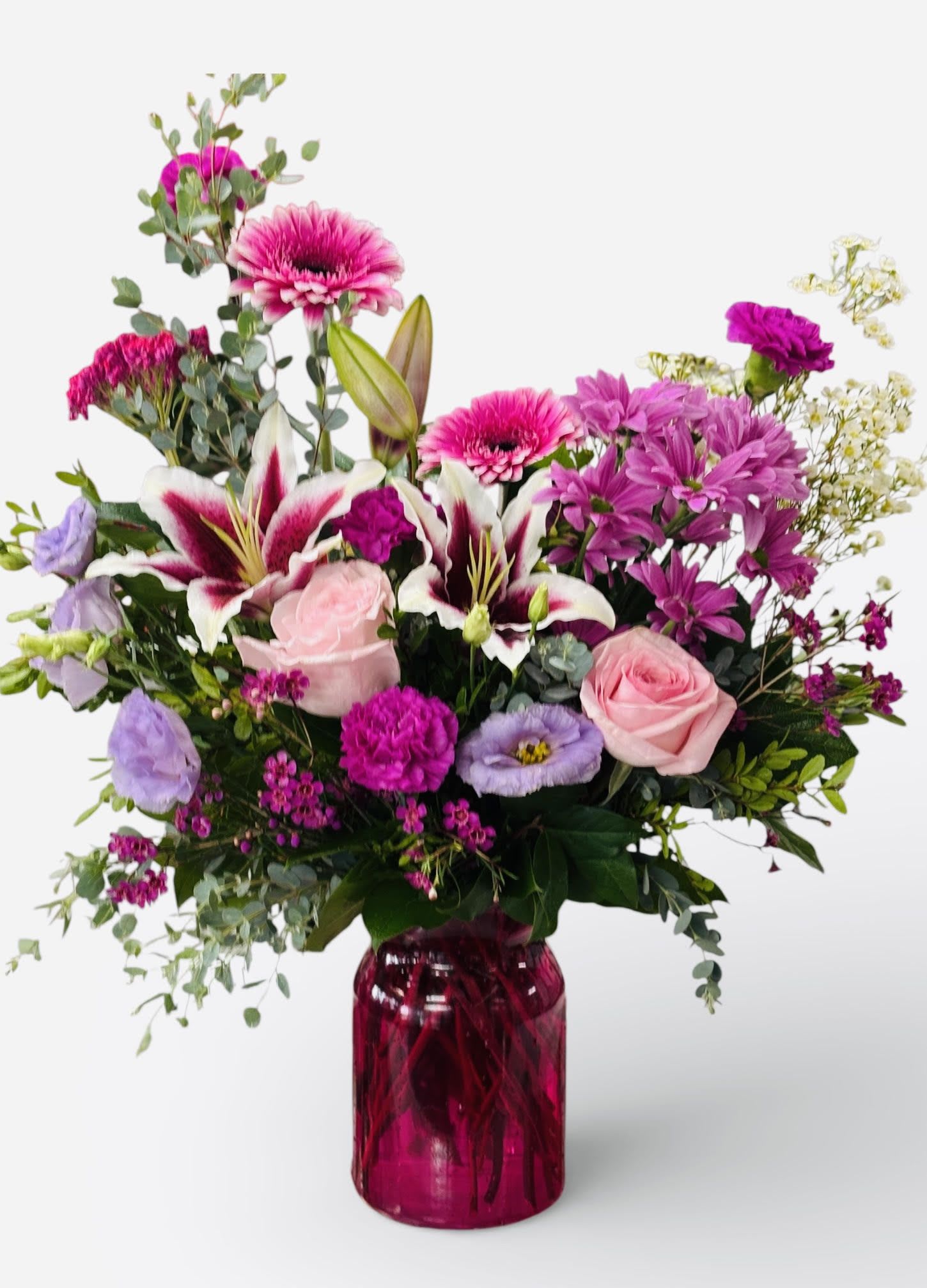 Bright pink and purple mixed flower arrangement with lilies and roses in a pink glass vase