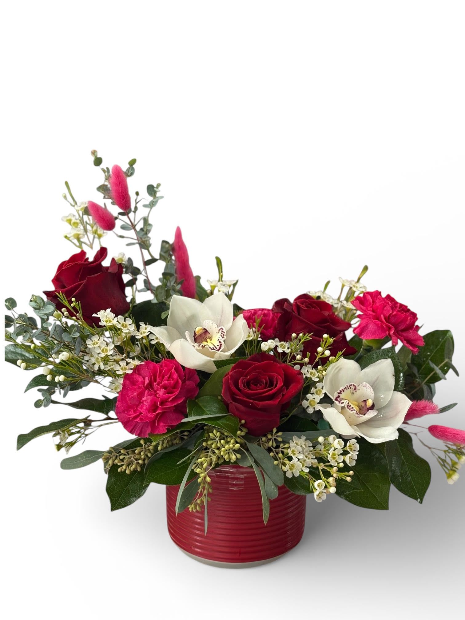 Low arrangement of red roses, hot pink carnations, and white orchids in a red ceramic vase