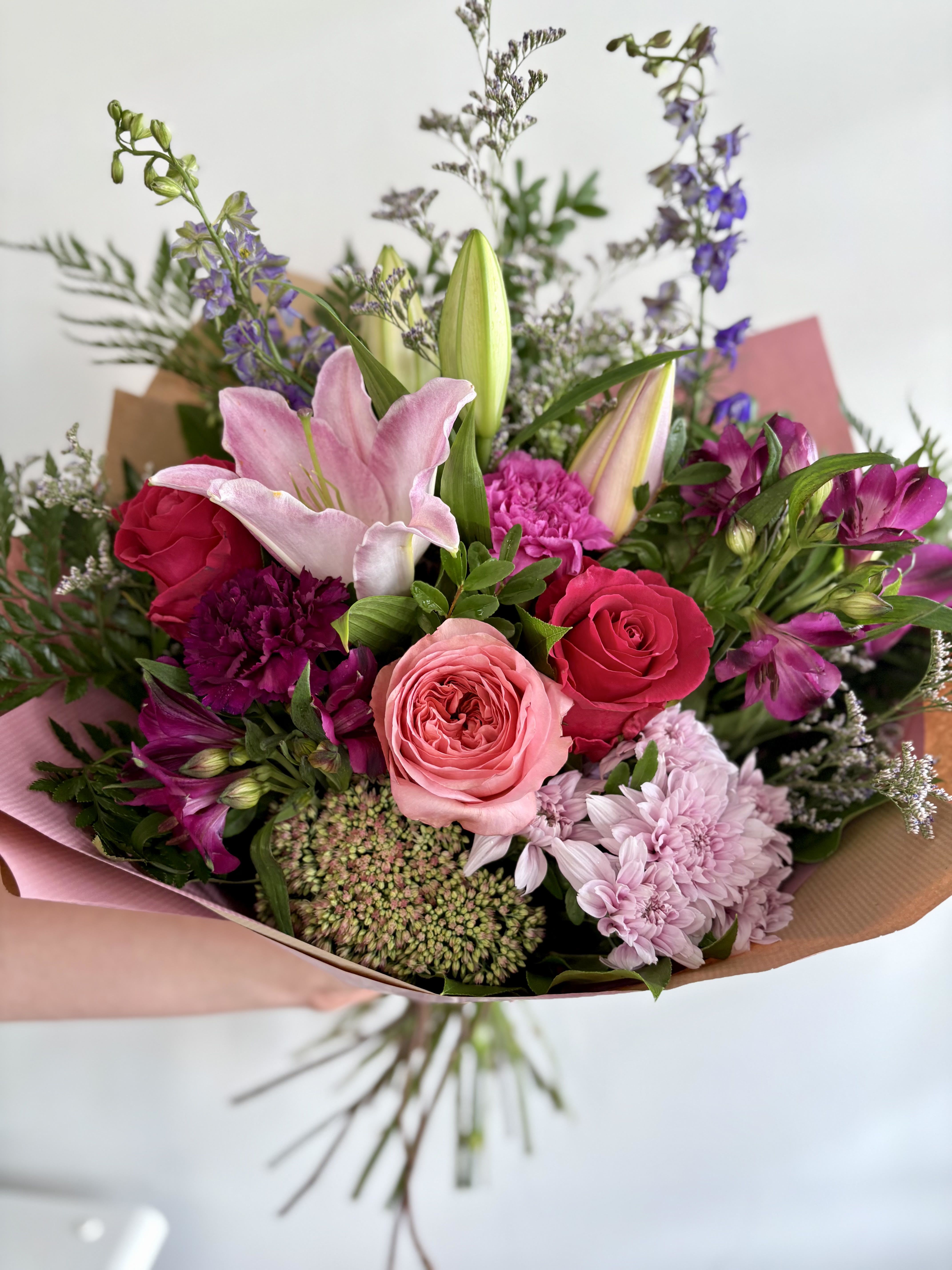 Hand-tied bouquet of pink lilies, roses, and mixed blooms wrapped in pink and kraft paper