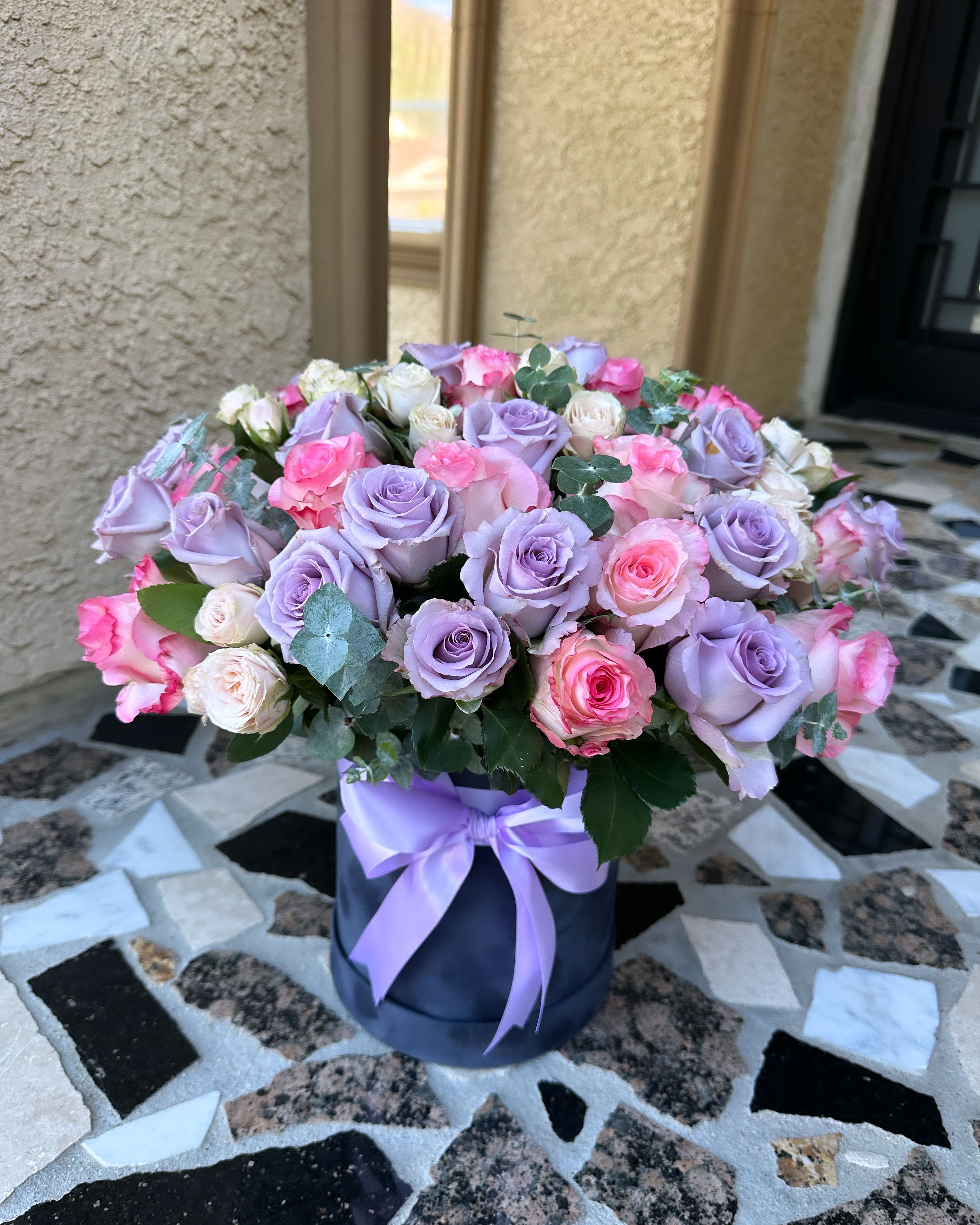 Lavender and pink roses arranged in a round box with a ribbon