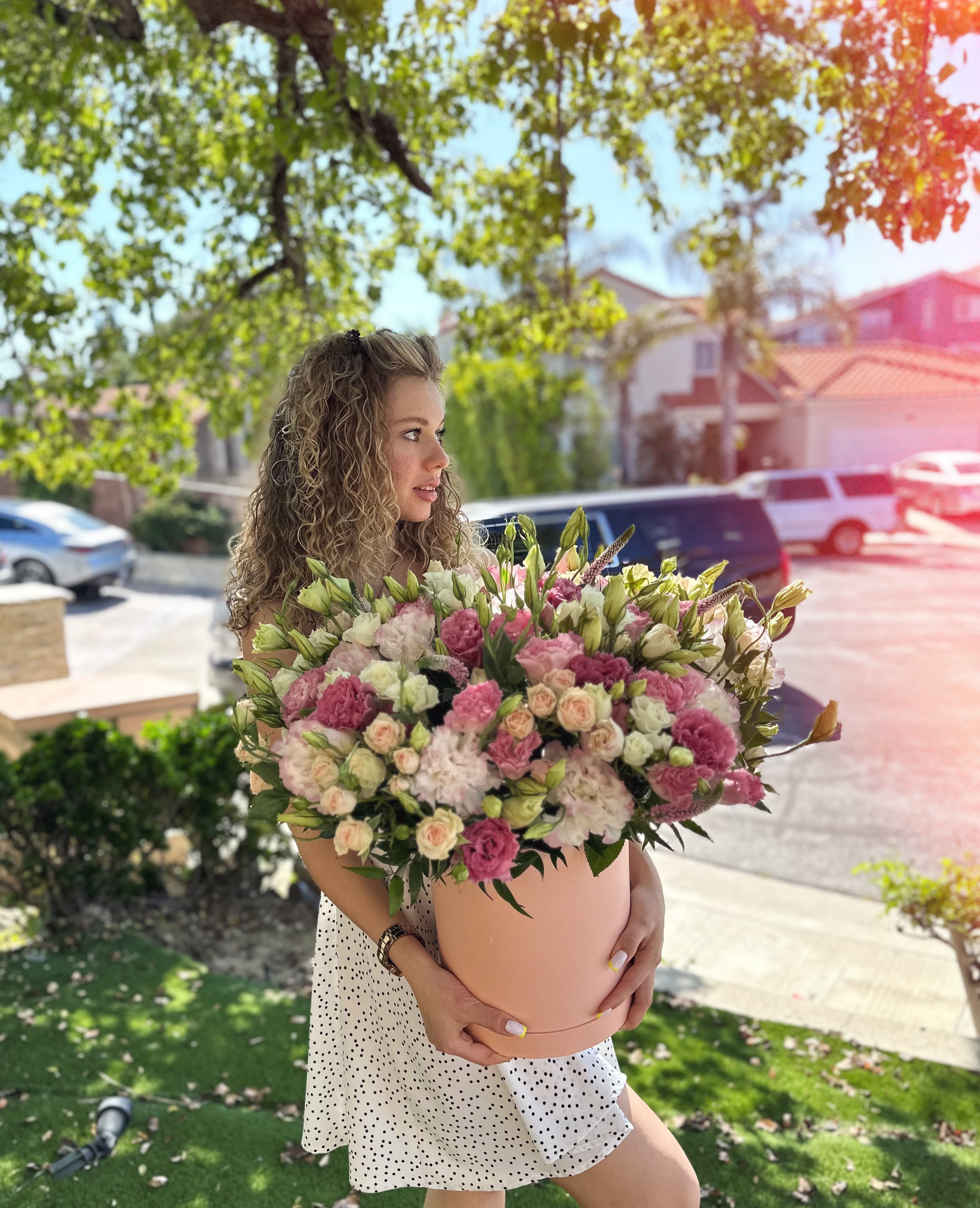 Woman holding a large pink and white flower arrangement in a round box