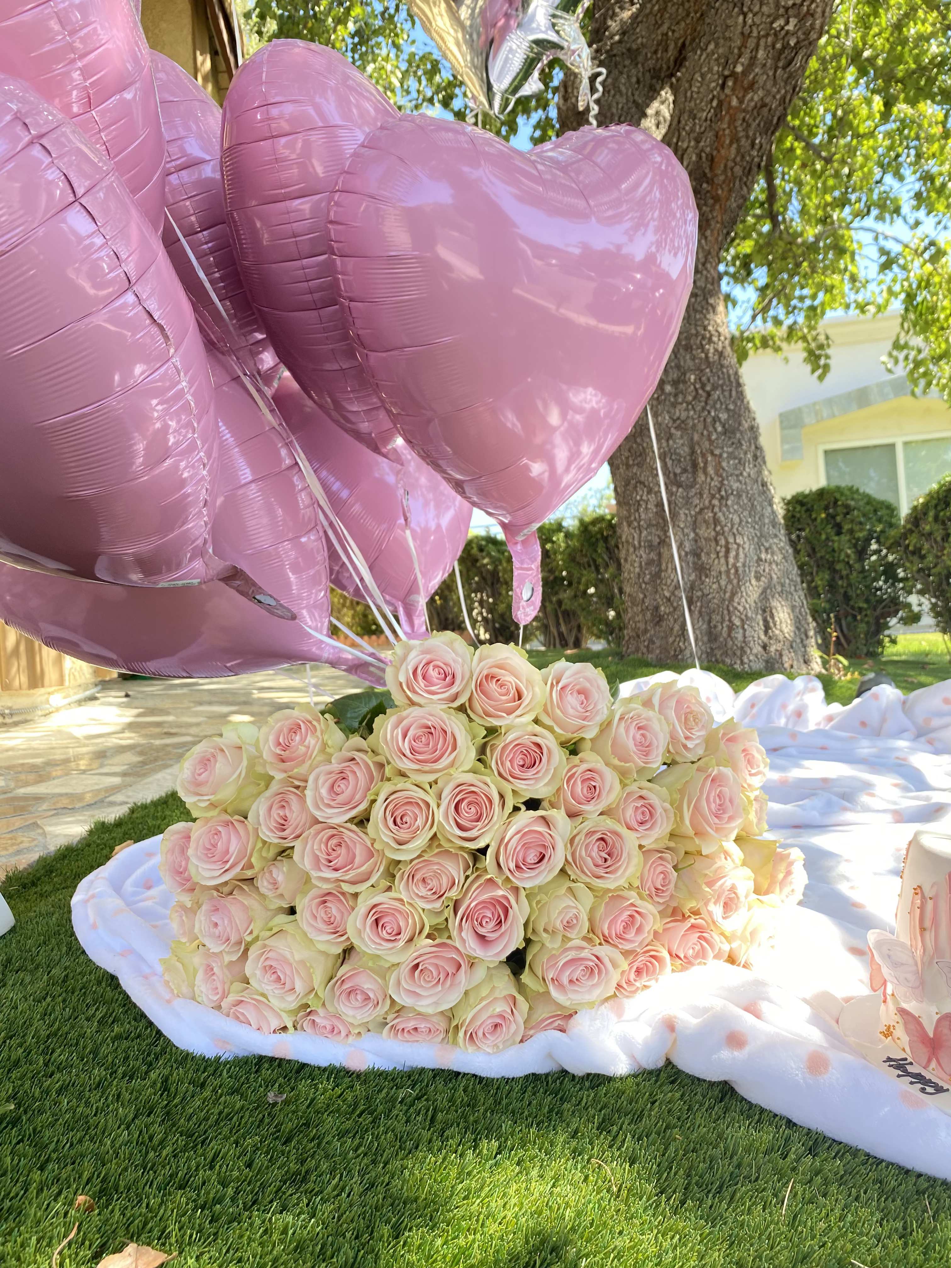 Pink heart balloons above a large bouquet of pale pink roses