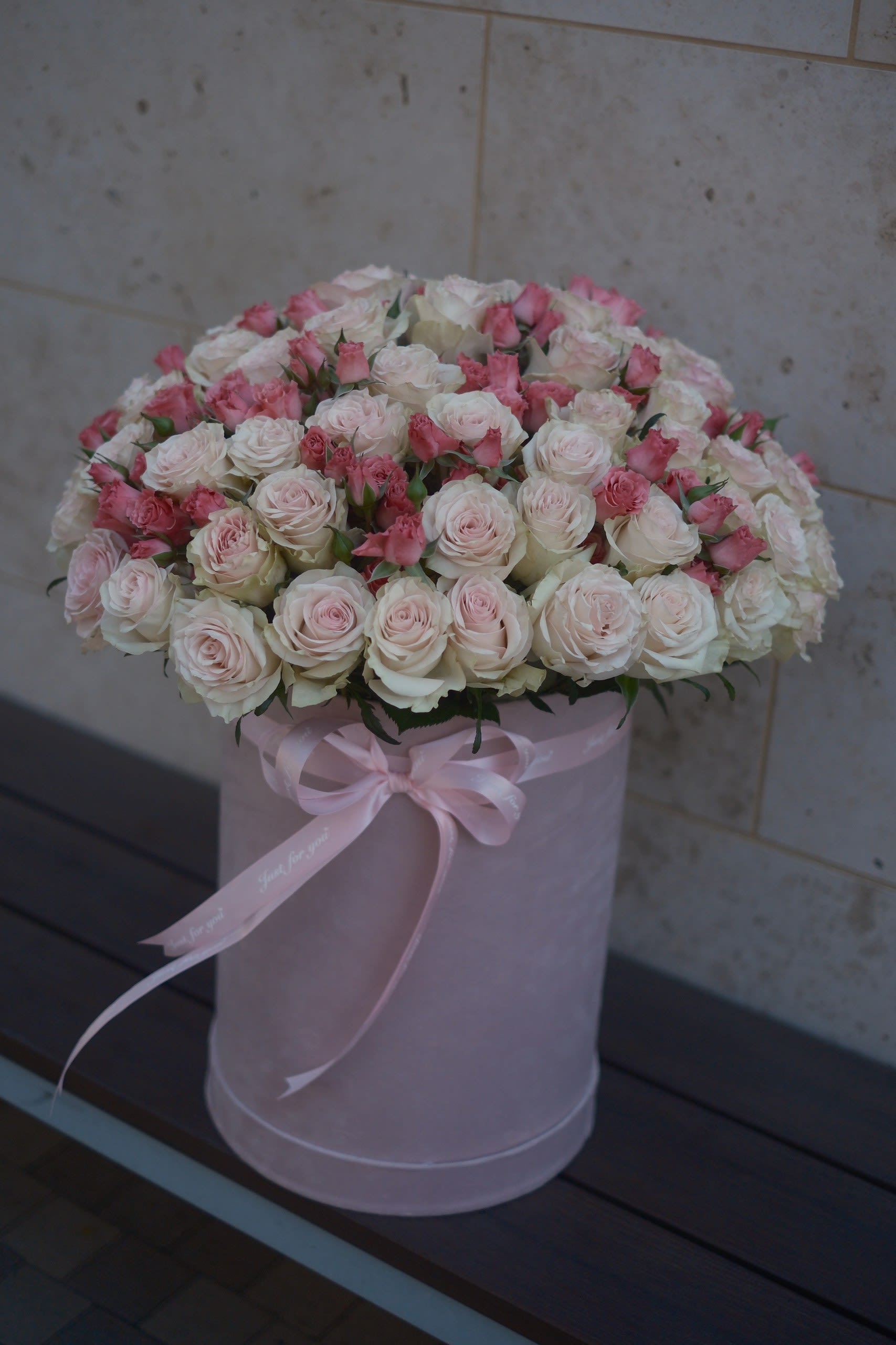 Pink and white roses arranged in a round hatbox with a ribbon bow