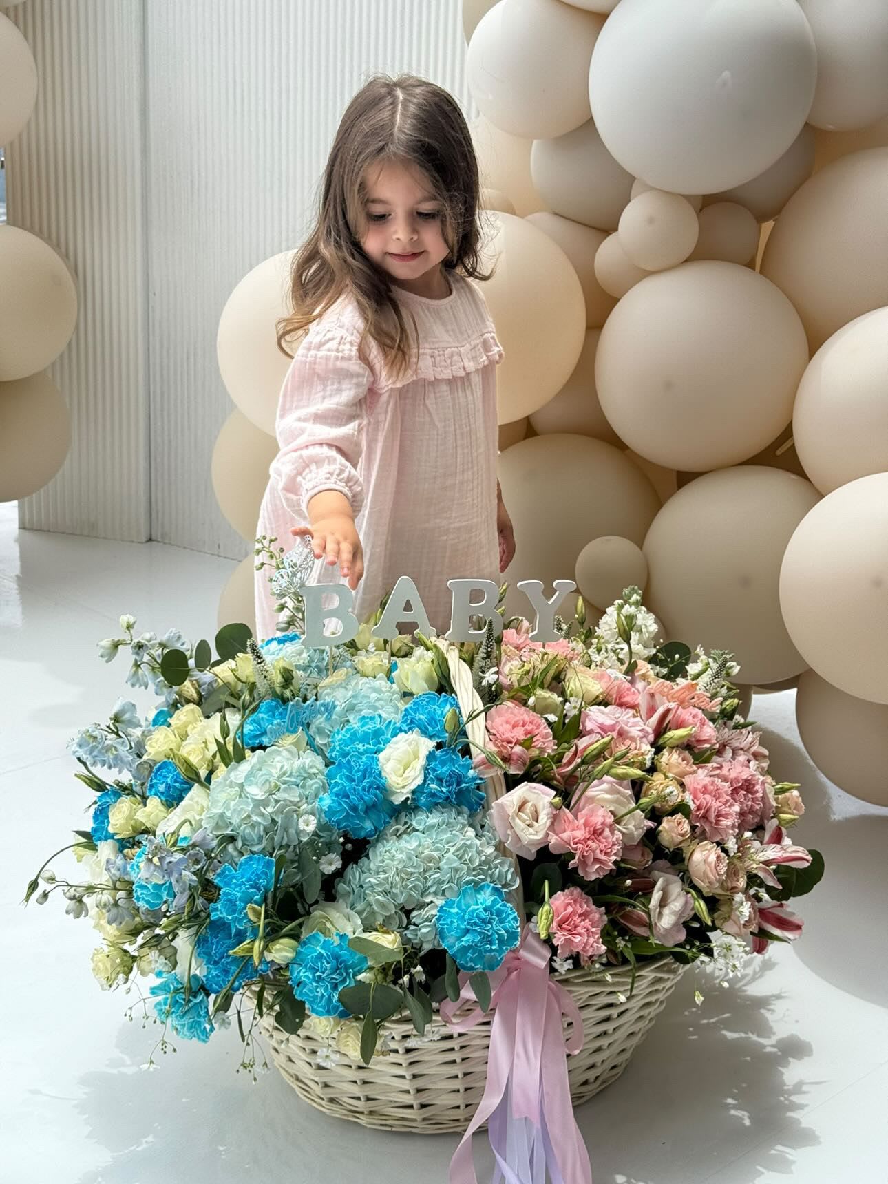 Large pastel flower basket with a BABY sign and a child standing behind it