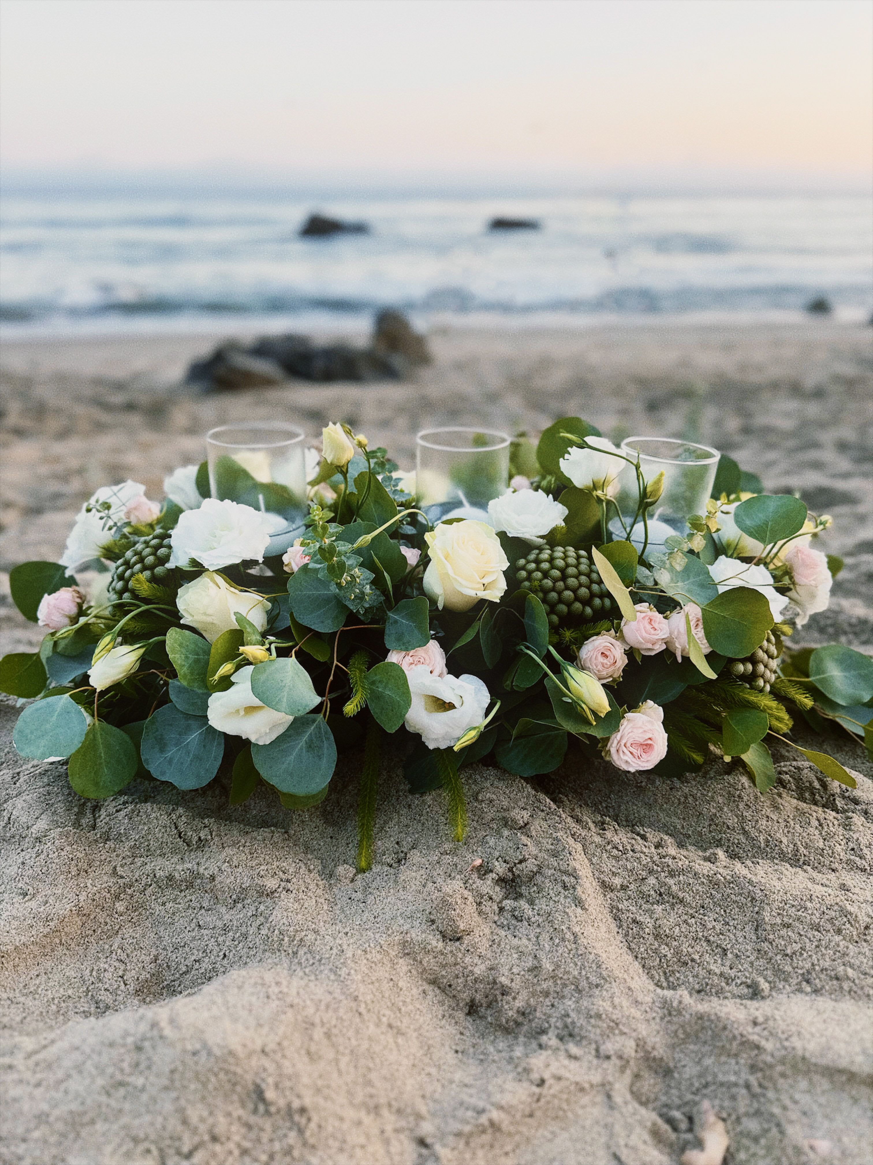 Low floral centerpiece with white and blush blooms on a beach
