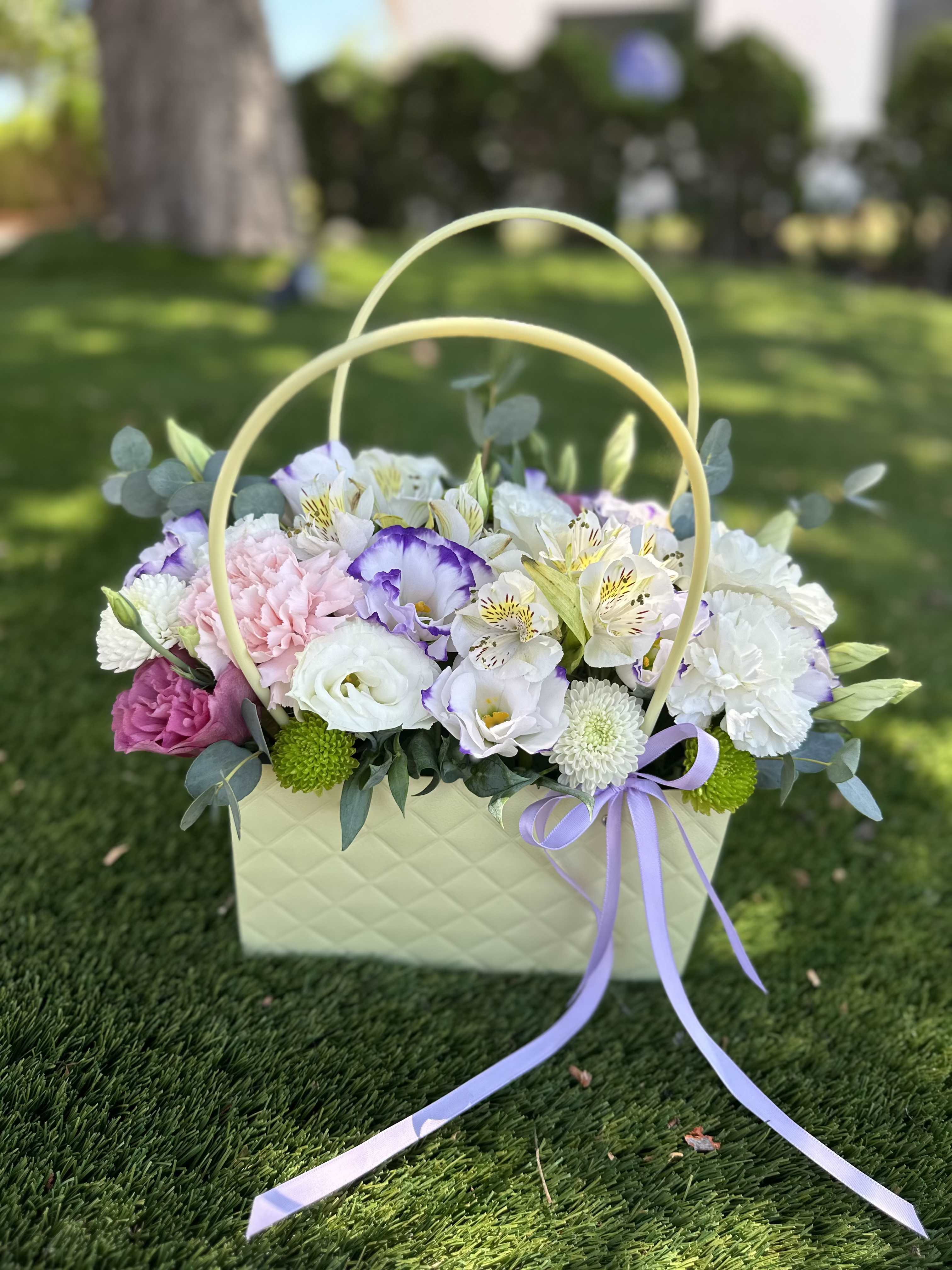 Basket of pastel flowers with a lavender ribbon on grass