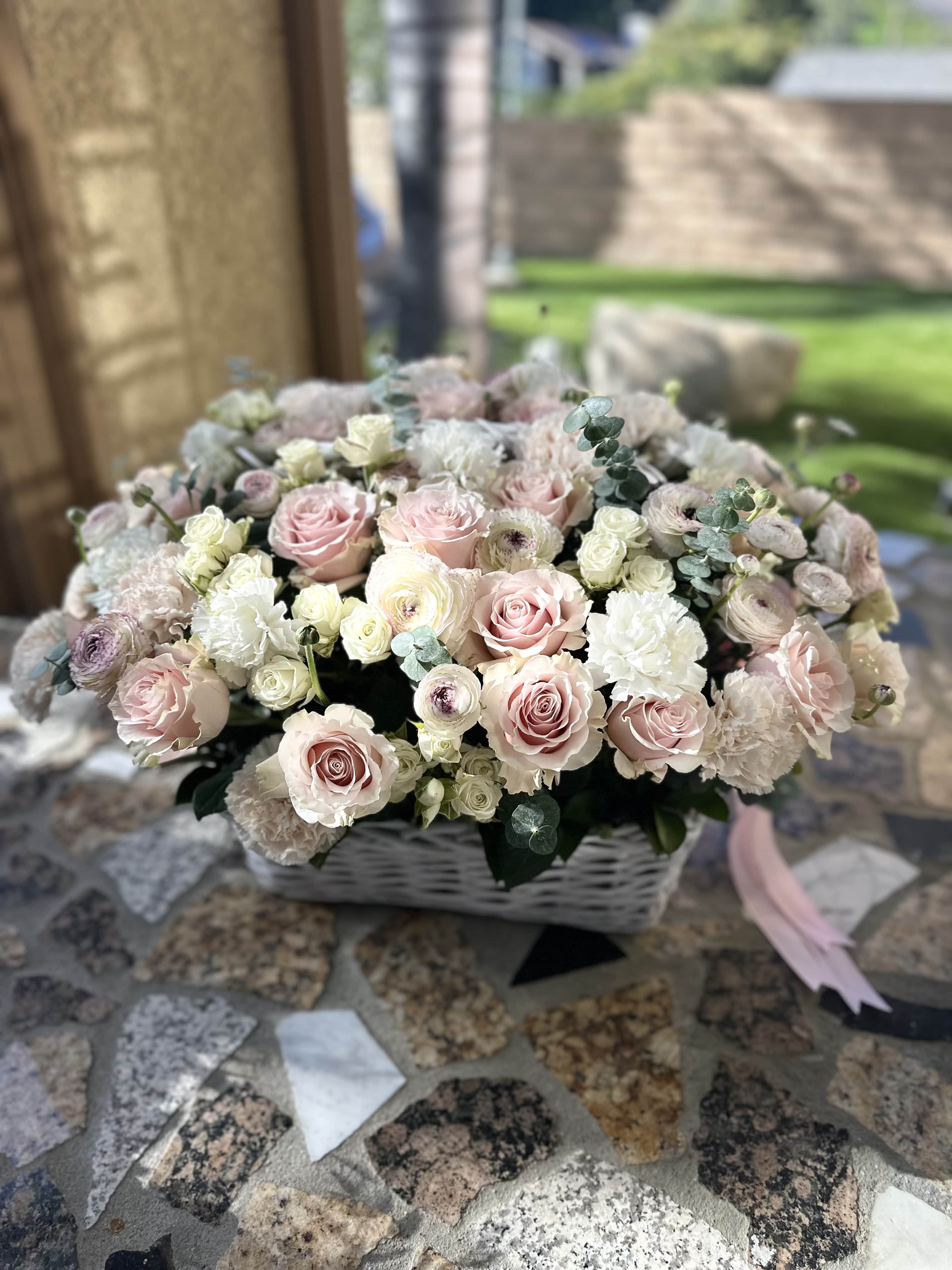 Basket arrangement of pale pink and white roses with soft filler flowers