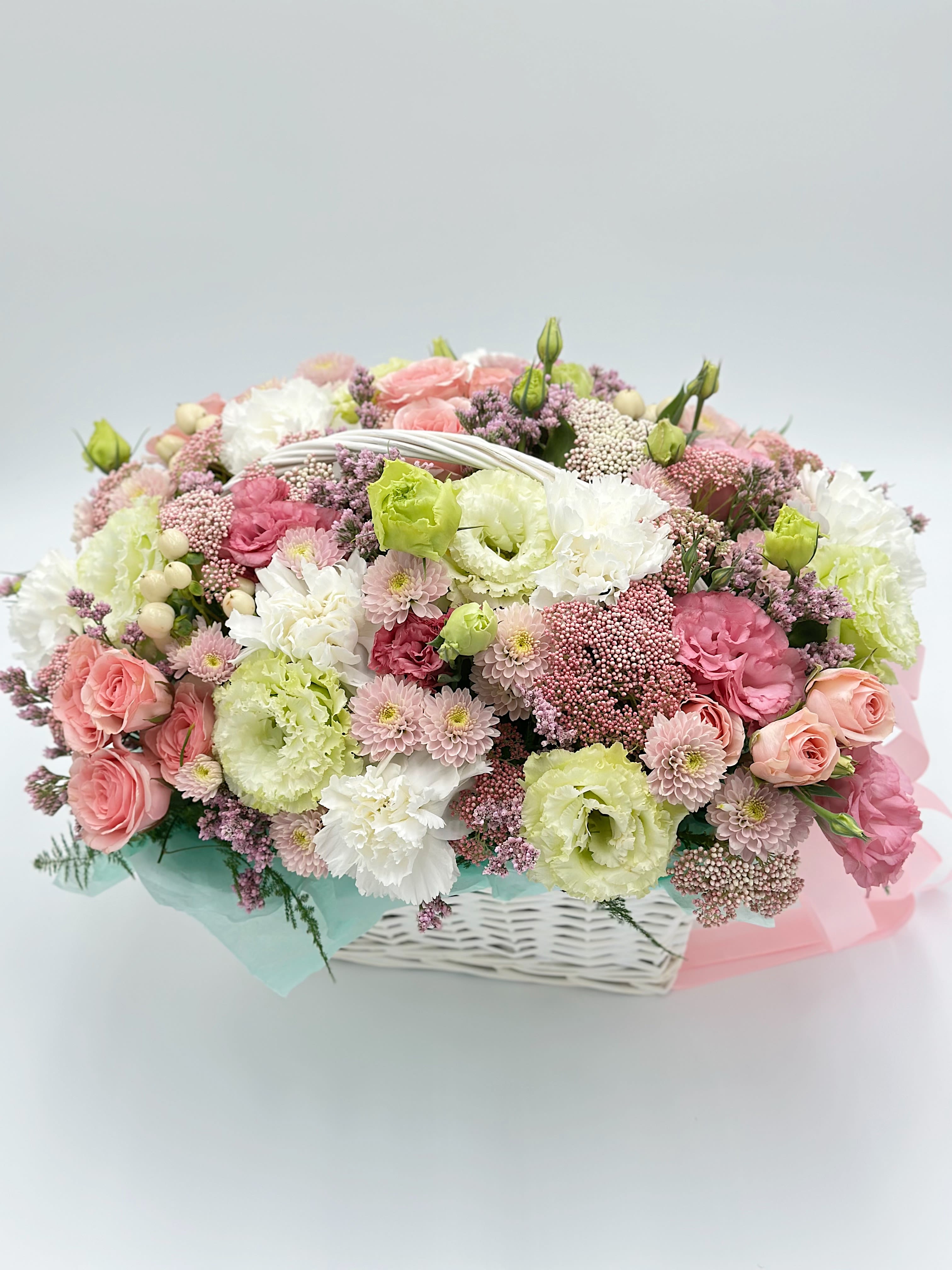 Pastel bouquet of pink, white, and green flowers in a white basket