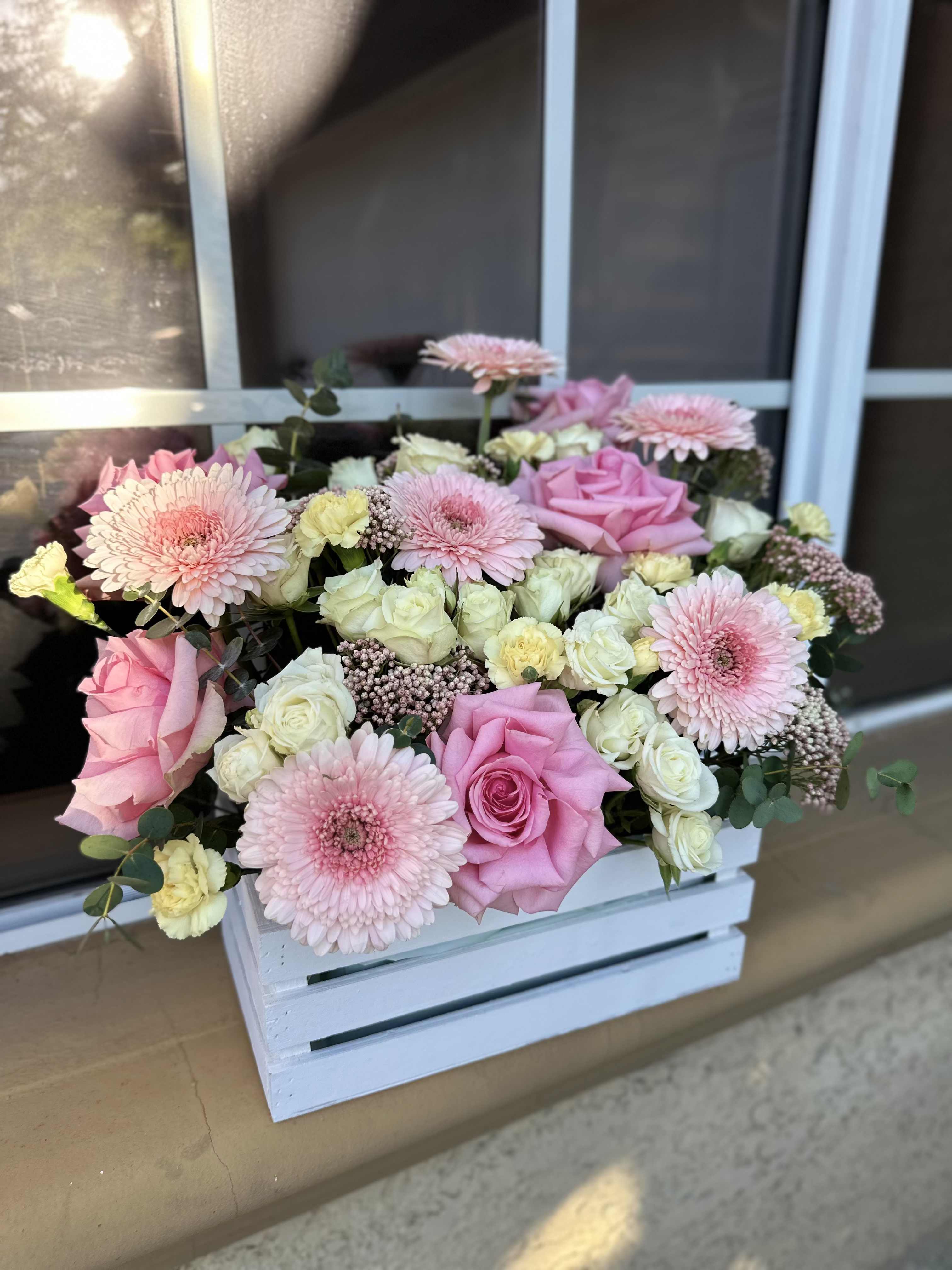 Pink roses and gerbera daisies arranged in a white wooden crate