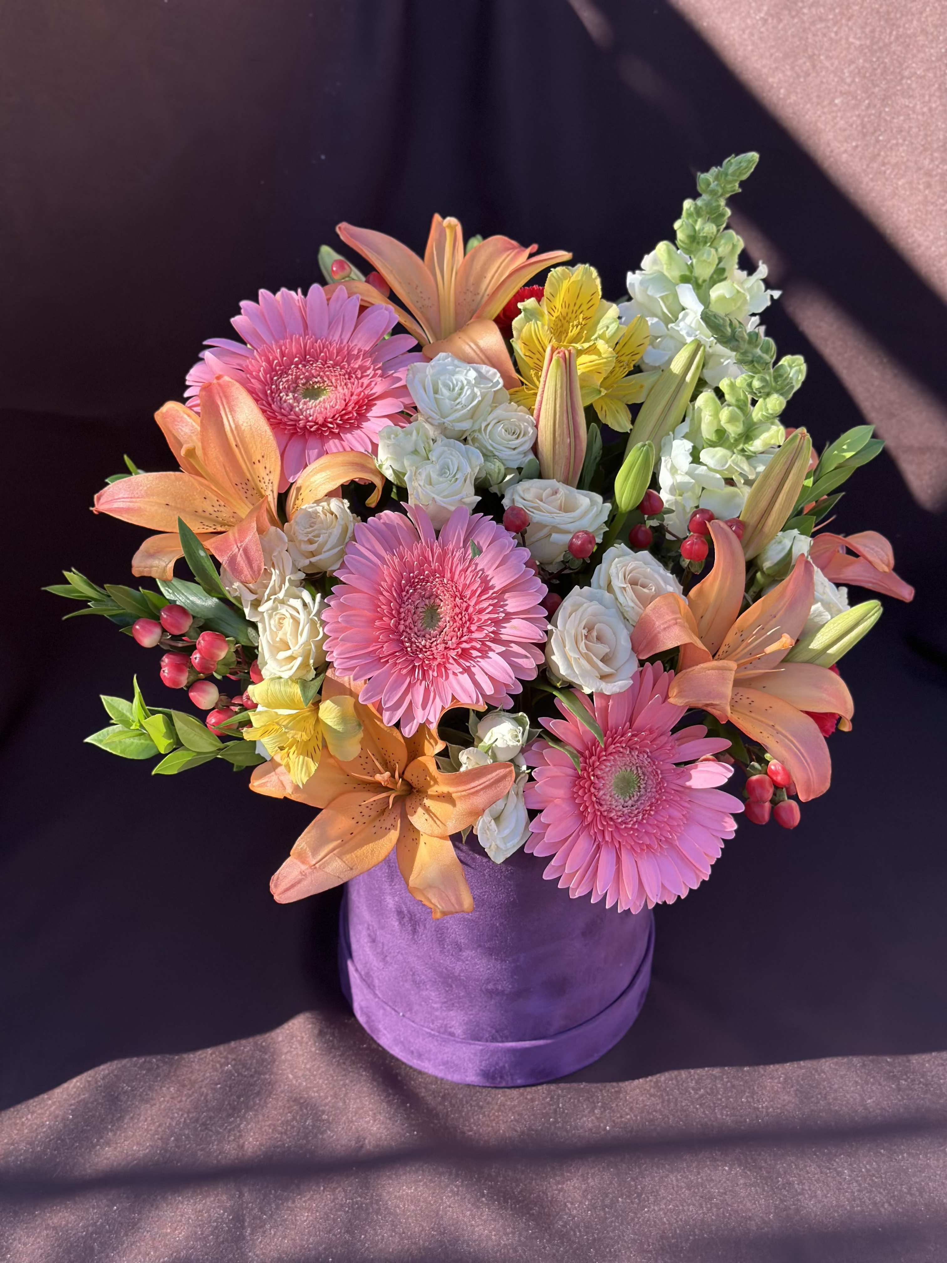 Pink gerberas, peach lilies, and white roses in a purple hat box