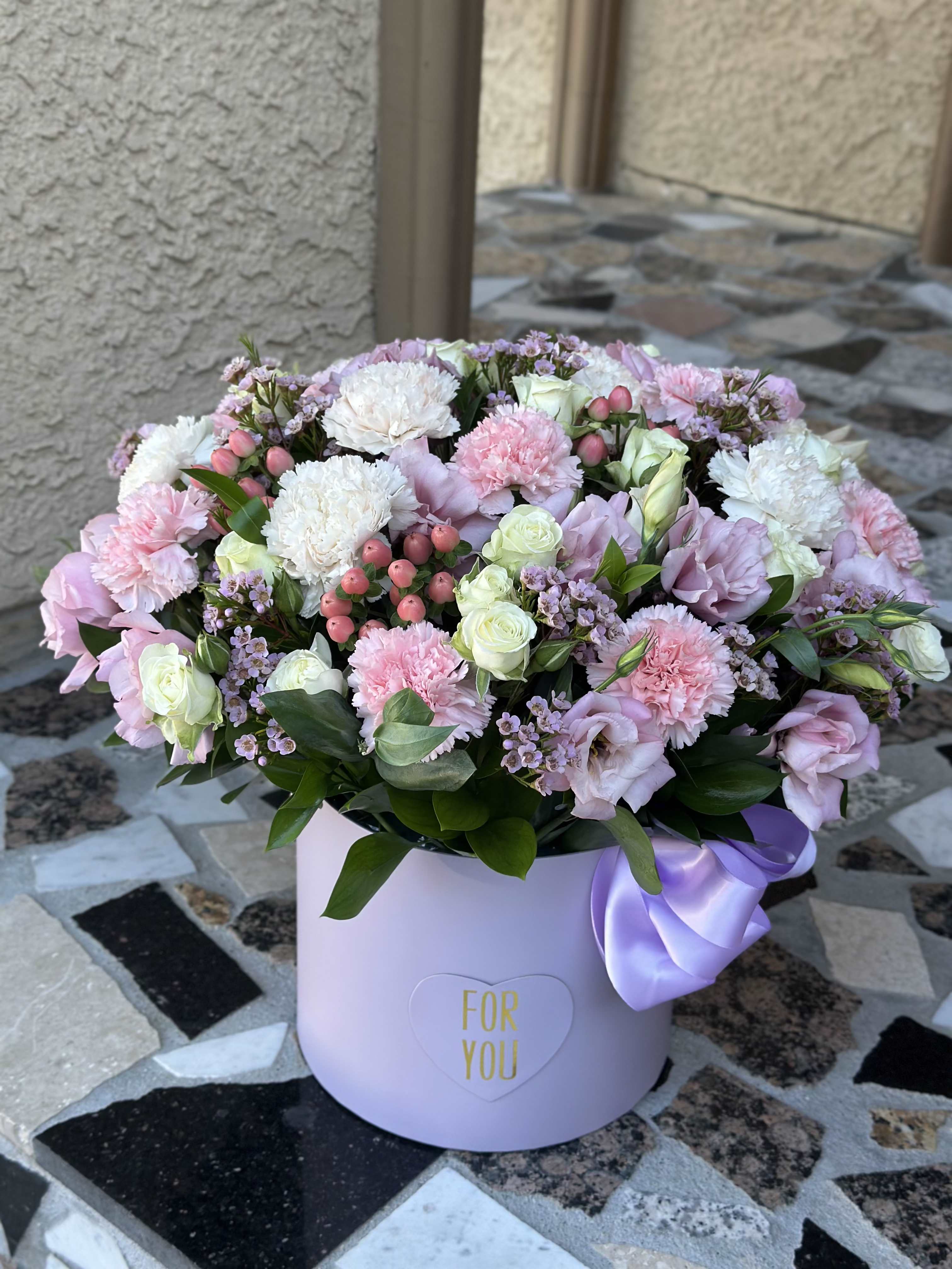 Pastel pink and white flower arrangement in a lavender hat box with a ribbon