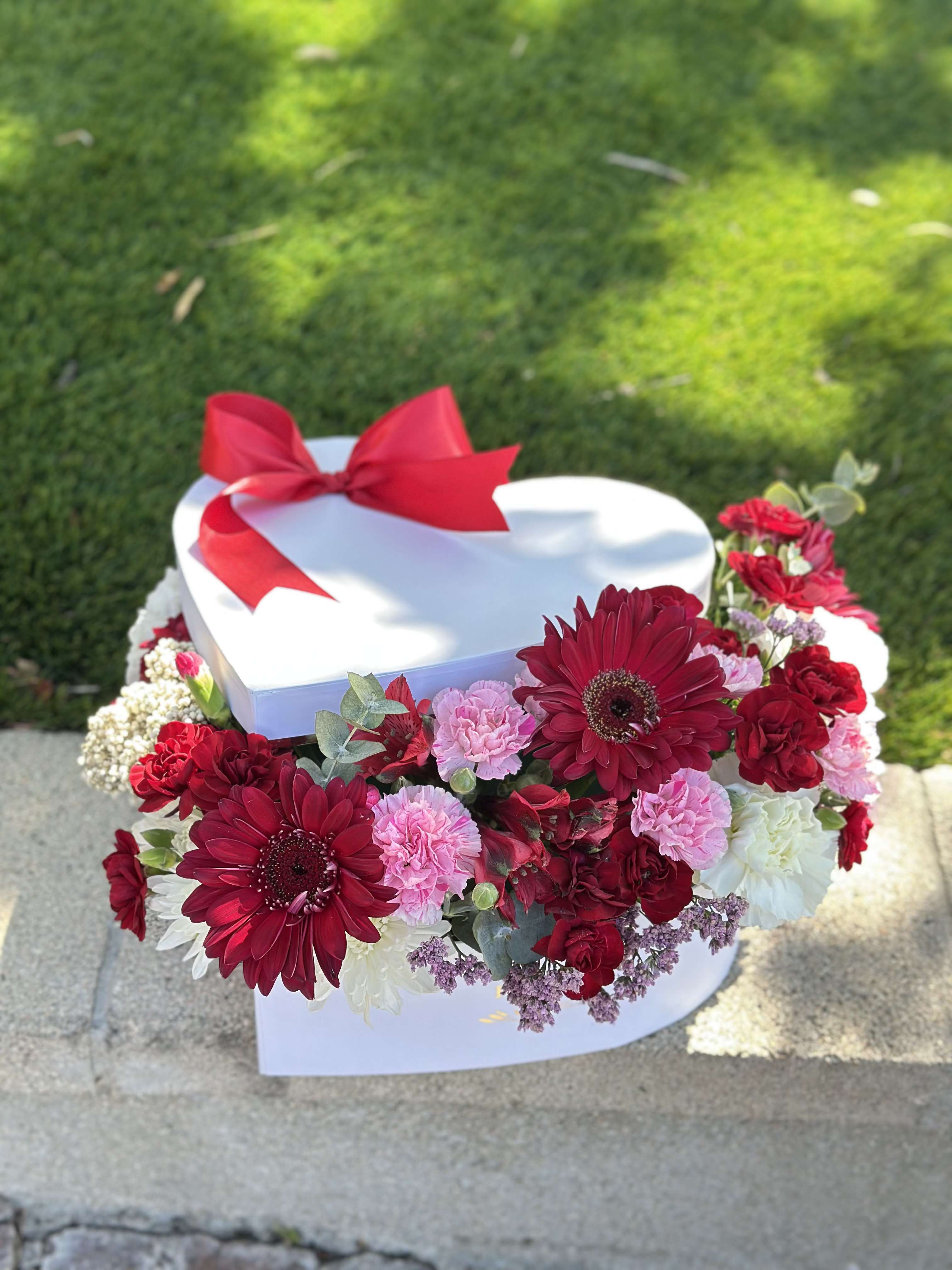 Heart-shaped white gift box with red ribbon and red, pink, and white flowers