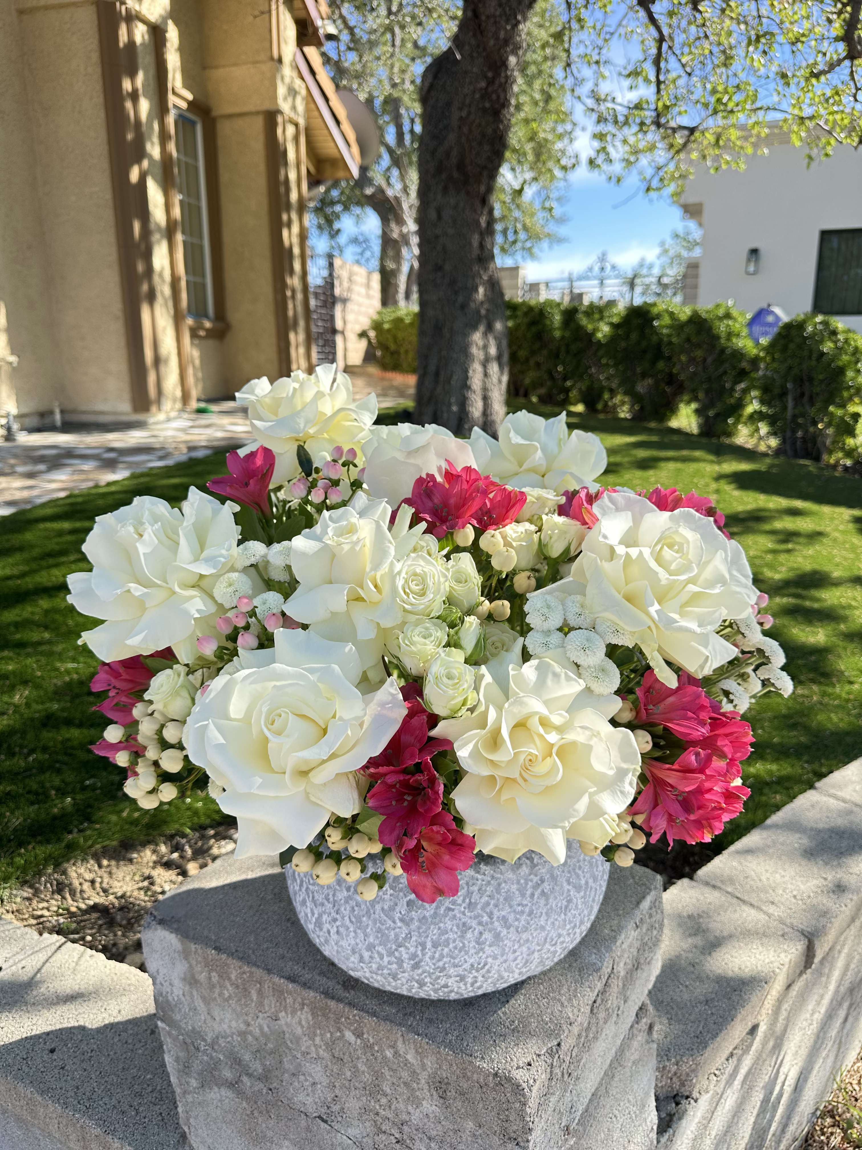 White roses and hot pink flowers arranged in a round gray vase