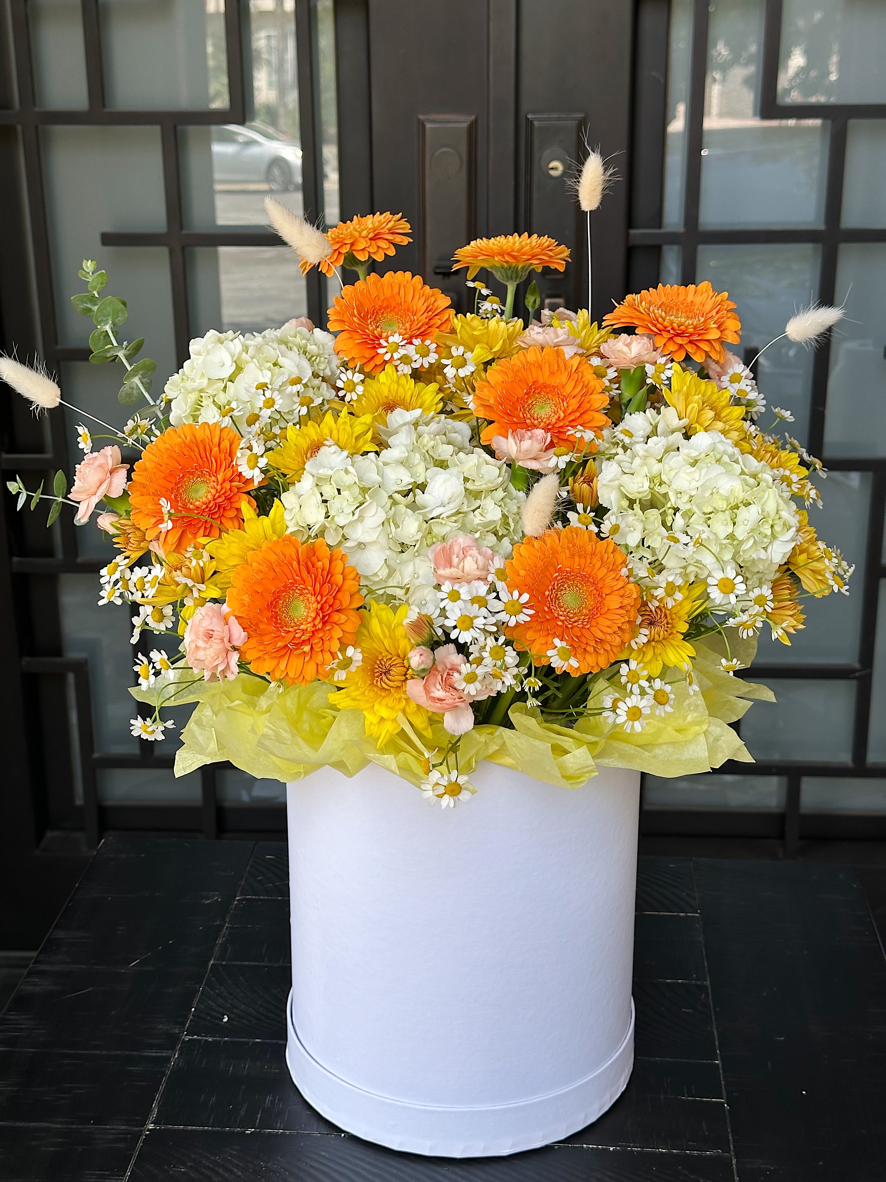 Bright mixed flower arrangement in a white box with orange and yellow blooms