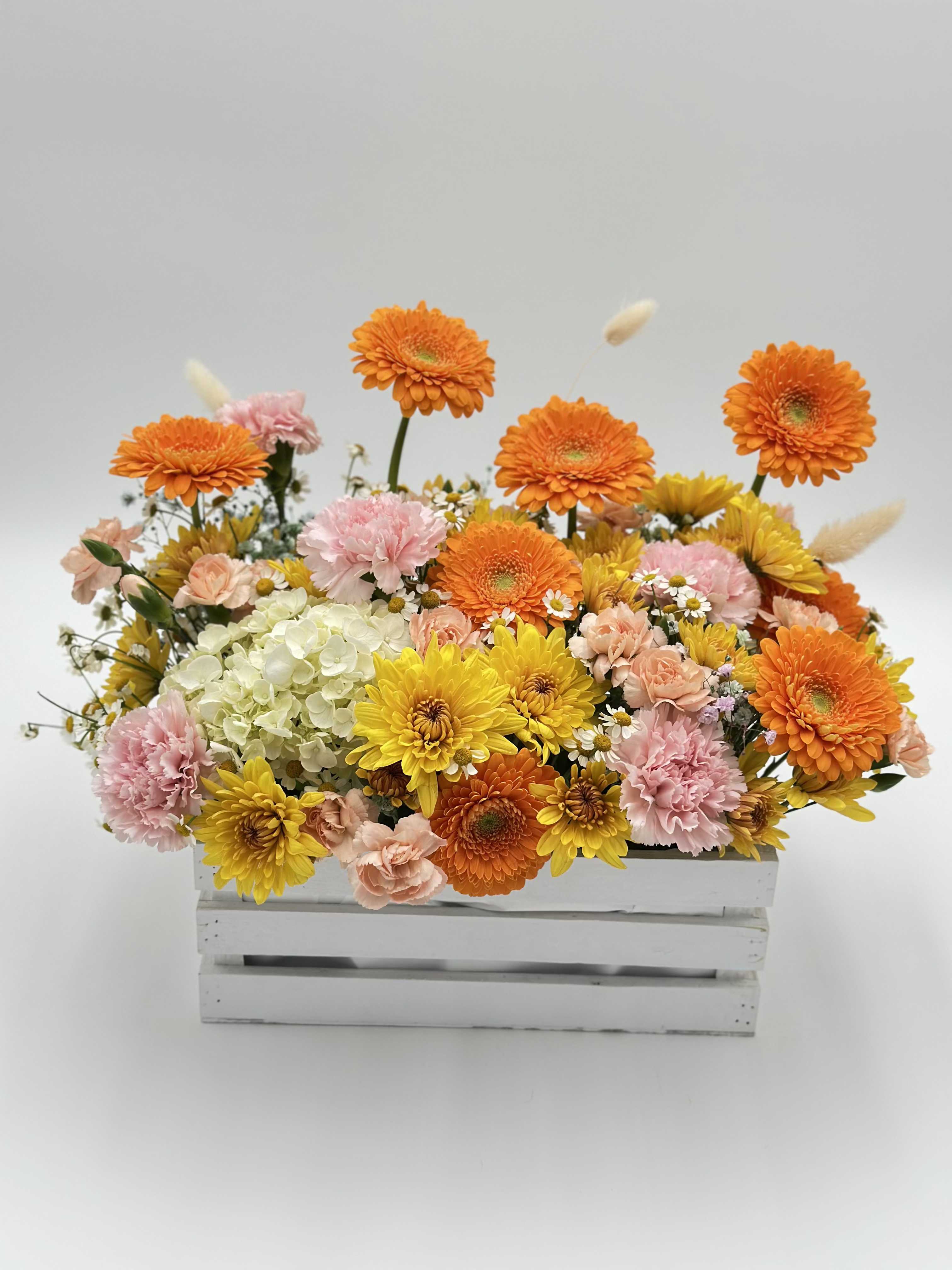 Bright mixed flower arrangement in a white wooden crate