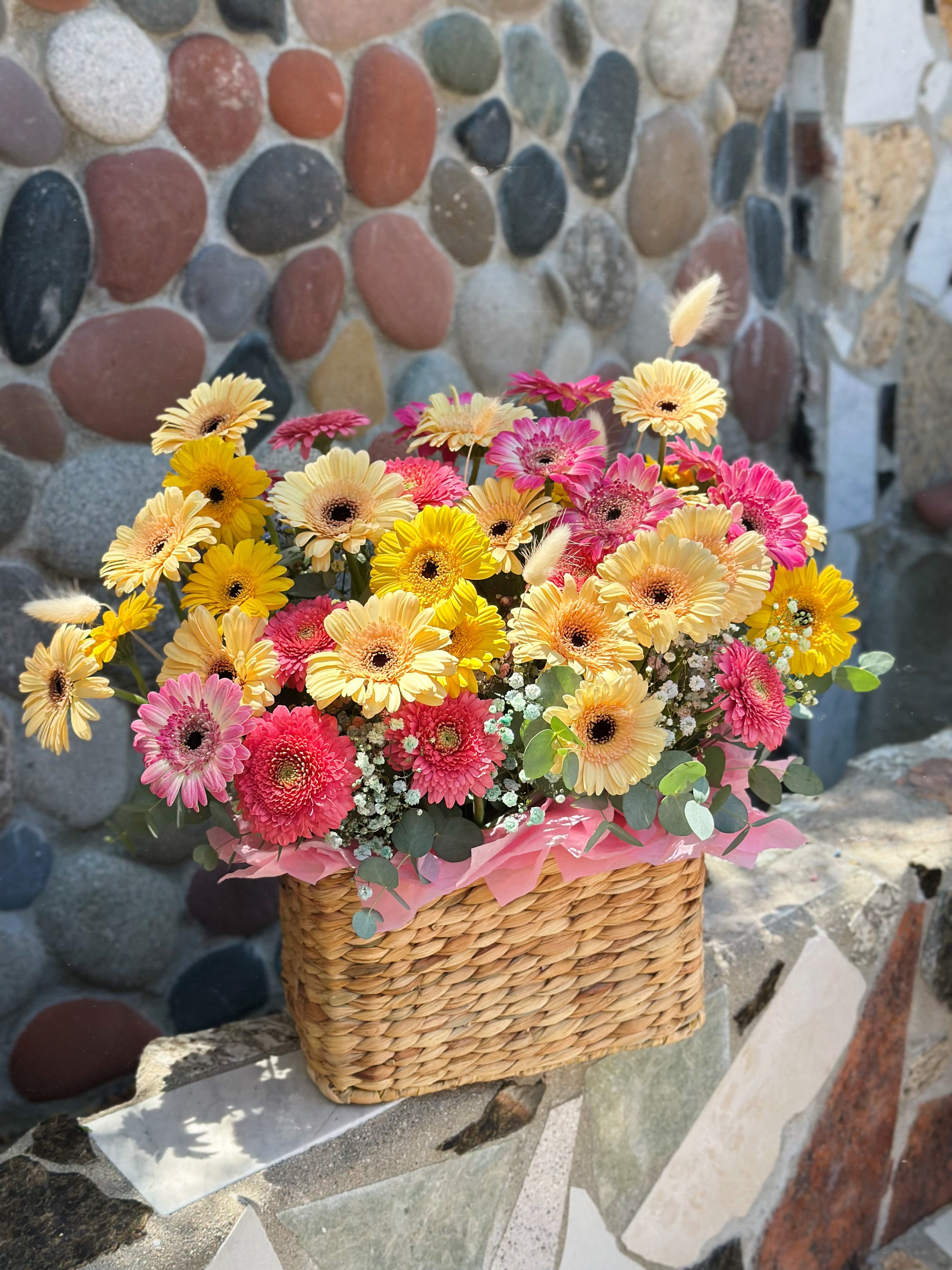 Mixed gerbera daisies in a woven basket with pink tissue paper