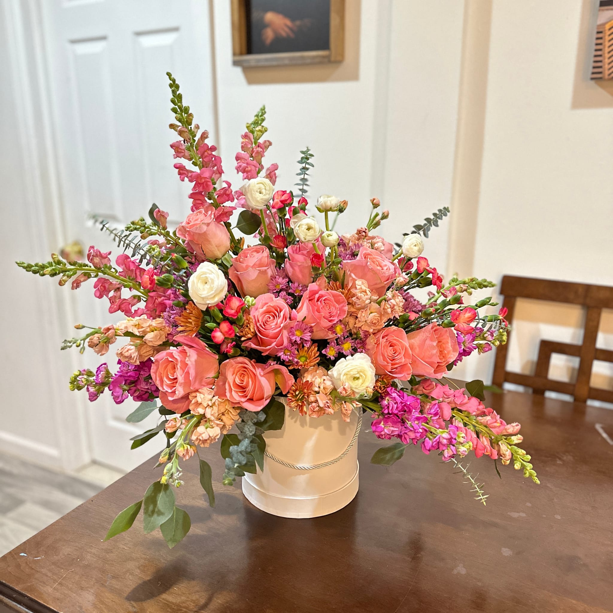 Pink and peach floral arrangement in a white hatbox-style container
