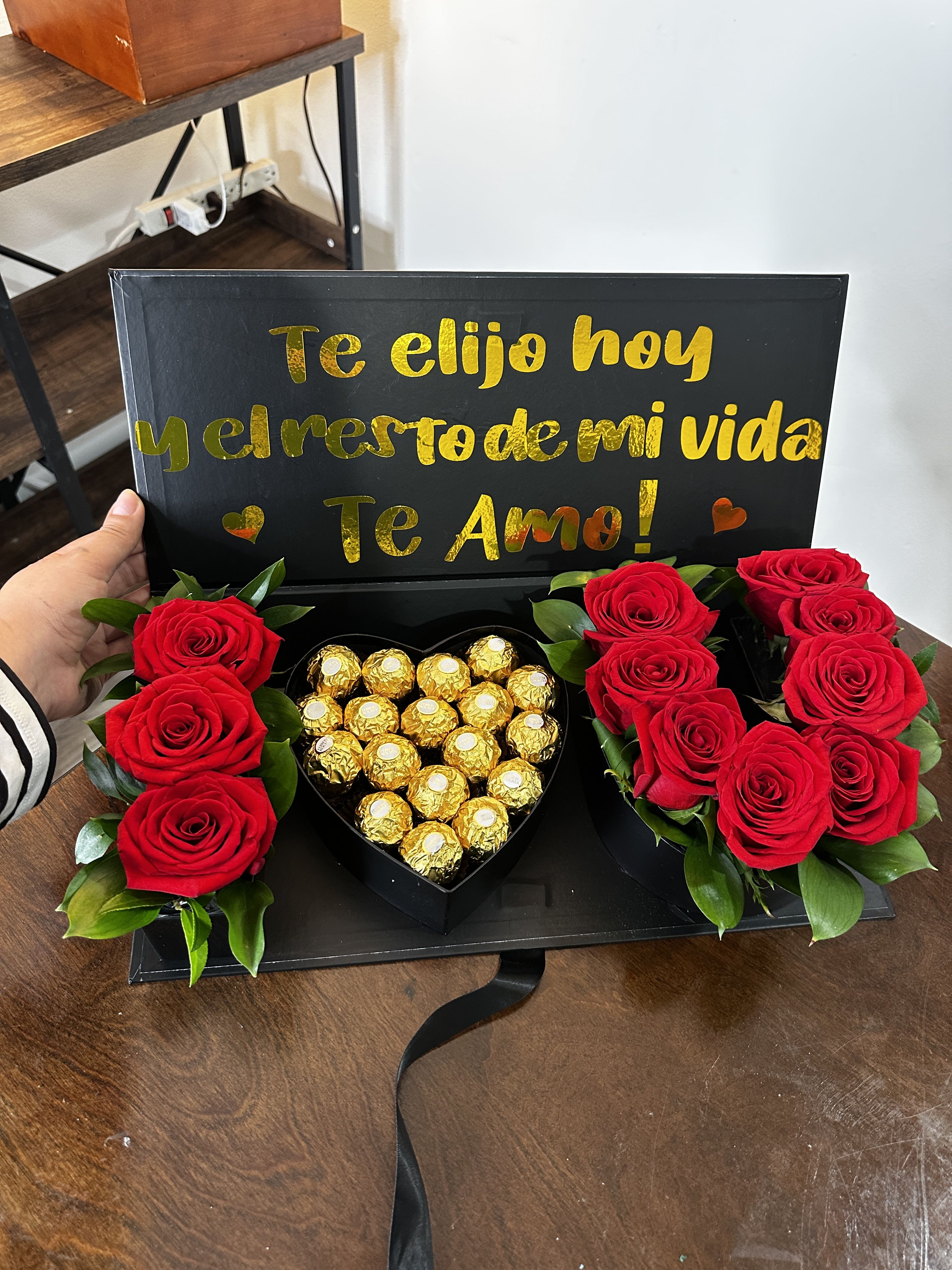 Red roses and gold-wrapped chocolates in a black gift box with a love message