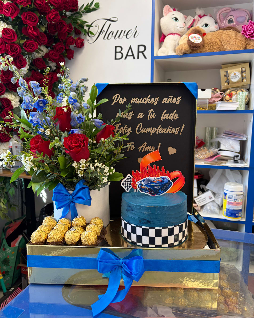 Red rose arrangement with blue flowers, chocolates, and a blue cake in a gift box