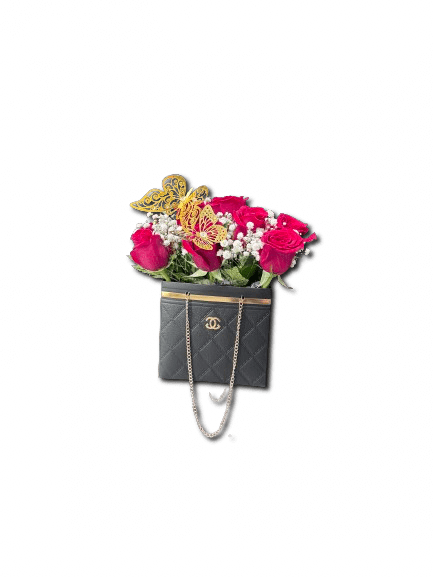 Red roses and white filler flowers arranged in a black quilted handbag with gold butterfly accents.