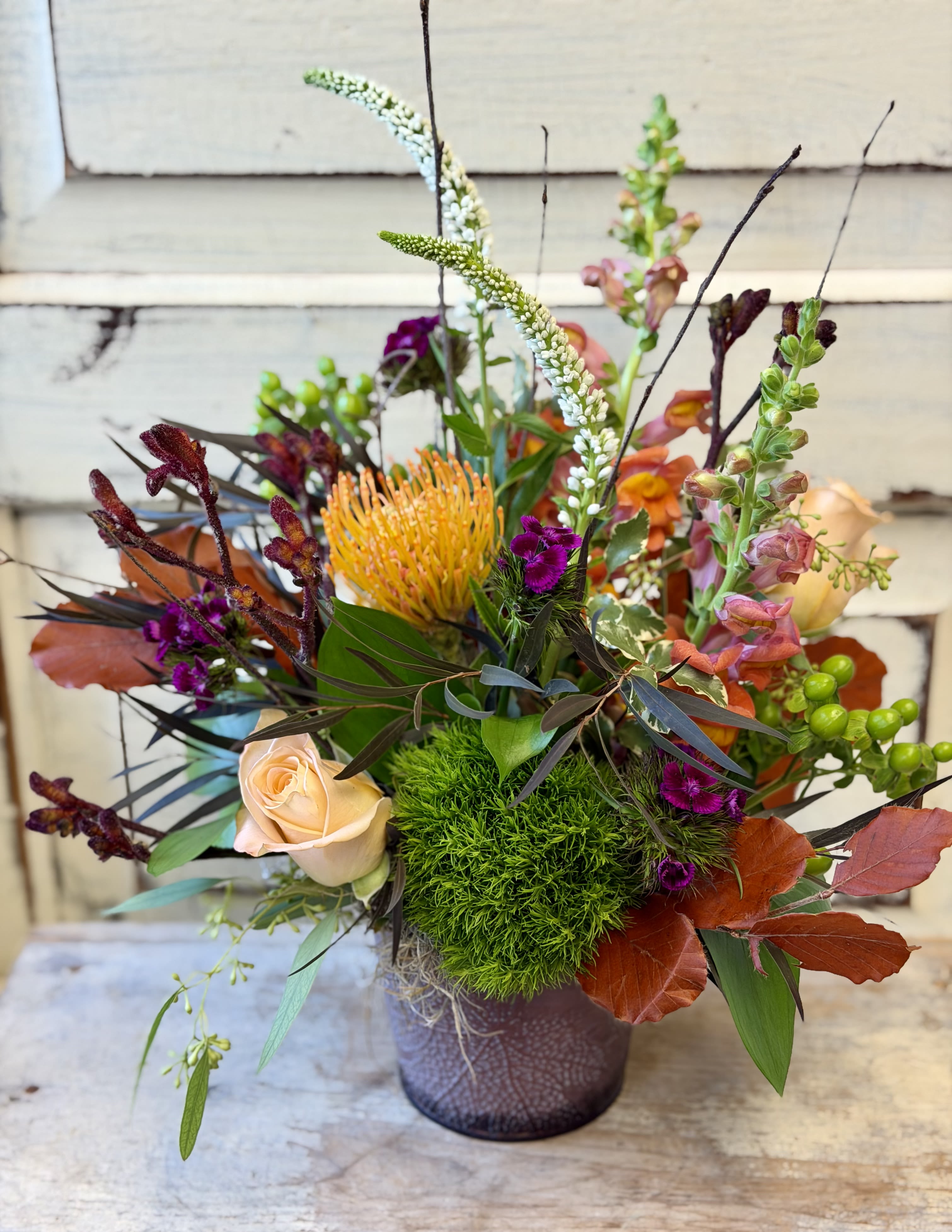Mixed floral arrangement in a purple vase with peach and orange blooms