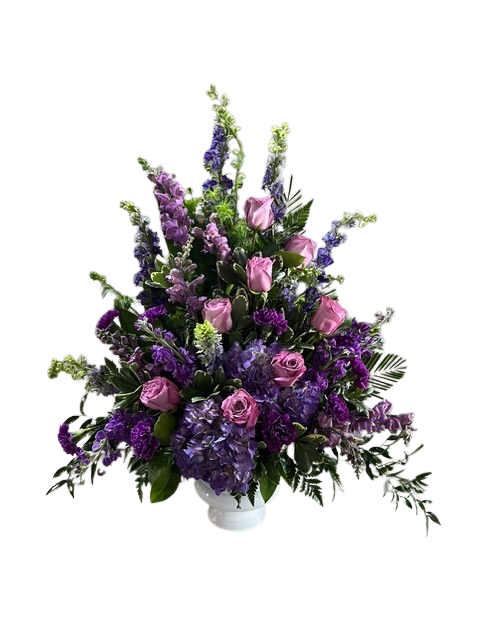 Lavender Horizon - Lavender and deep purple blooms form a lush, layered tribute in this sympathy flower arrangement, with lavender roses rising through the center to convey gentle warmth. As a sympathy arrangement it reads as respectful and consoling, yet its romantic palette also suits anniversaries, birthdays, or a thoughtful "thinking of you" gesture for someone you want to comfort.  Rounded hydrangea clusters create a full, textured base while tall snapdragon-like spires add graceful height; mixed roses and other seasonal blooms fill the composition for rich color depth. The flowers arrive arranged in a clean white ceramic vase that keeps the look formal and easy to place in a home or funeral setting. Care: keep fresh water in the vase, trim stems occasionally, and place away from direct heat to prolong blooms.  As similar as possible. Designer may make appropriate changes based on flower availability. 