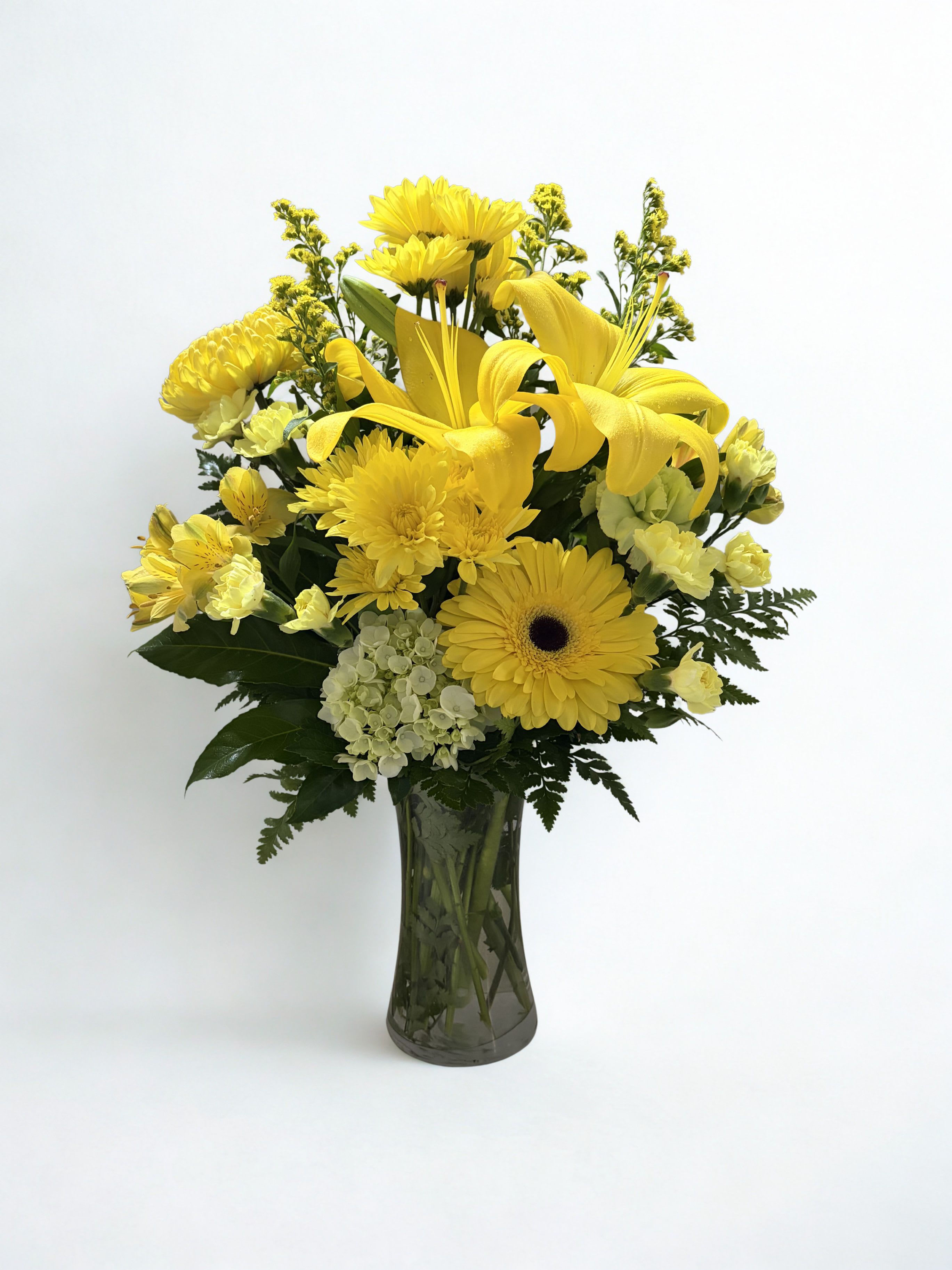 Golden Meadow  - Sunlit yellow lilies and gerbera daisies take center stage in this cheerful flower arrangement, making Marigold Meadow an ideal birthday bouquet or spring "just because" surprise that says thank you with sunshine. The upright, full composition feels bright and uplifting-perfect for the person you want to make smile.  A layered mix of yellow lilies, gerbera daisies, chrysanthemums, creamy white hydrangea, and alstroemeria sits in a glass vase, with deep green foliage and soft white accents for contrast and texture. Compact and easy to place, it arrives ready to display and brings fresh, sunny color to mantels, desks, or bedside tables.