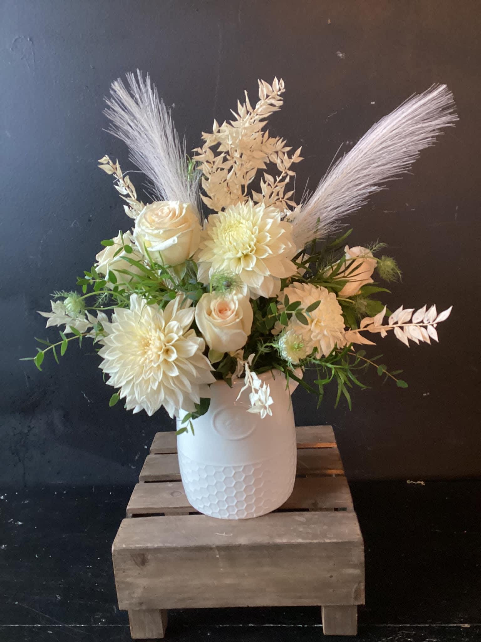 White floral arrangement in a textured white vase with feathery accents