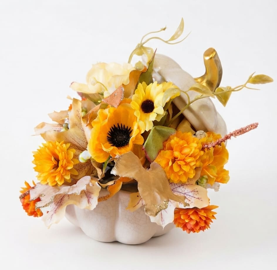 Orange and yellow floral arrangement in a white pumpkin container