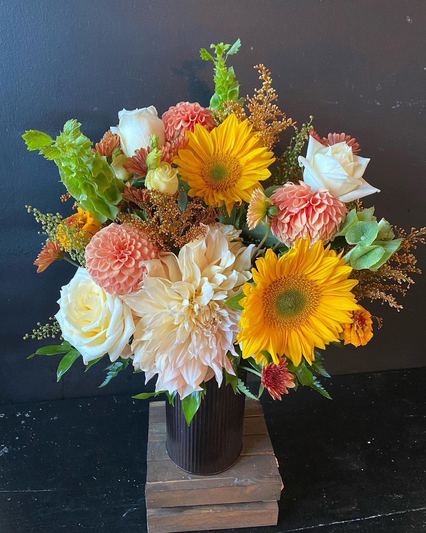 Bouquet of sunflowers, white roses, and peach dahlias in a dark vase