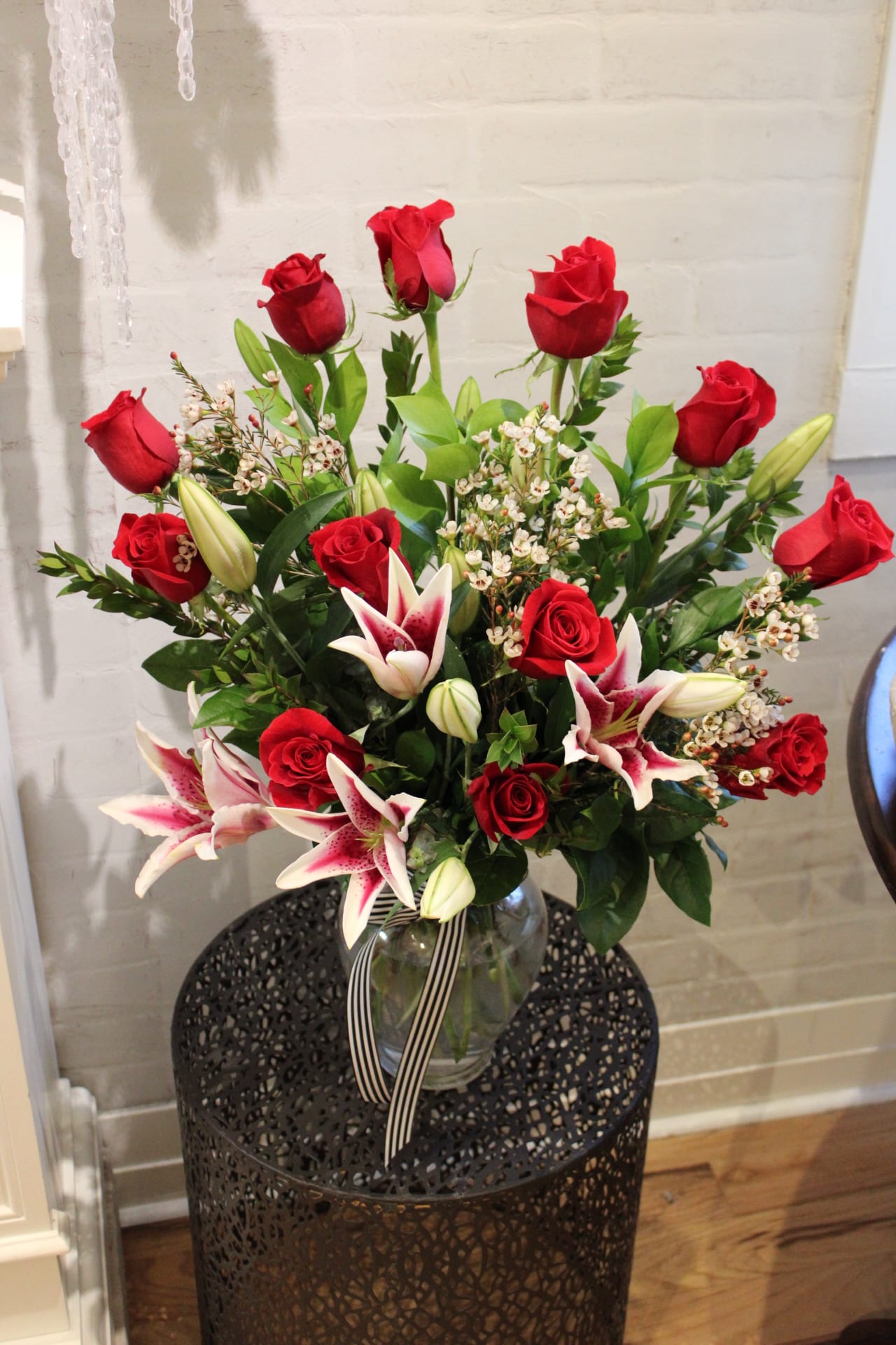 Red roses and pink lilies arranged in a glass vase with a striped ribbon.