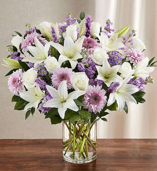 Sincerest Sorrow  Lavender &amp; White - Let a deeply heartfelt sentiment be delivered in true form. Our lush, bountiful bouquet of lavender and white blooms features an elegant mix of roses, lilies and cremones, hand-designed inside a classic clear glass vase. When sent to a service or to the home of family or friends, it makes a genuinely heartwarming gesture.