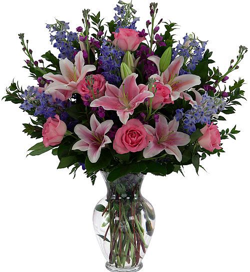 Pink lilies and roses with blue flowers in a clear glass vase