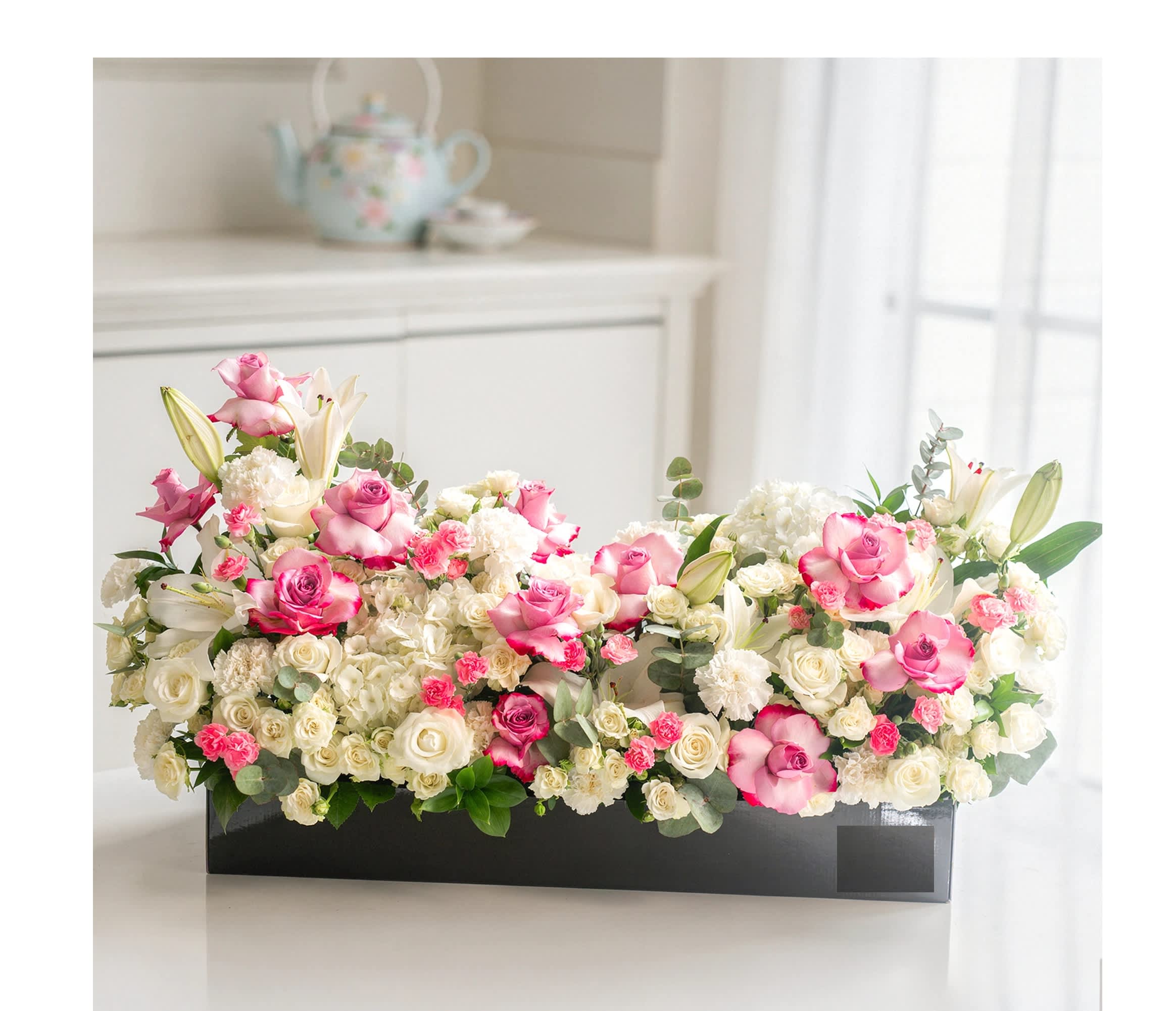 Pink and white roses with lilies arranged in a black rectangular box