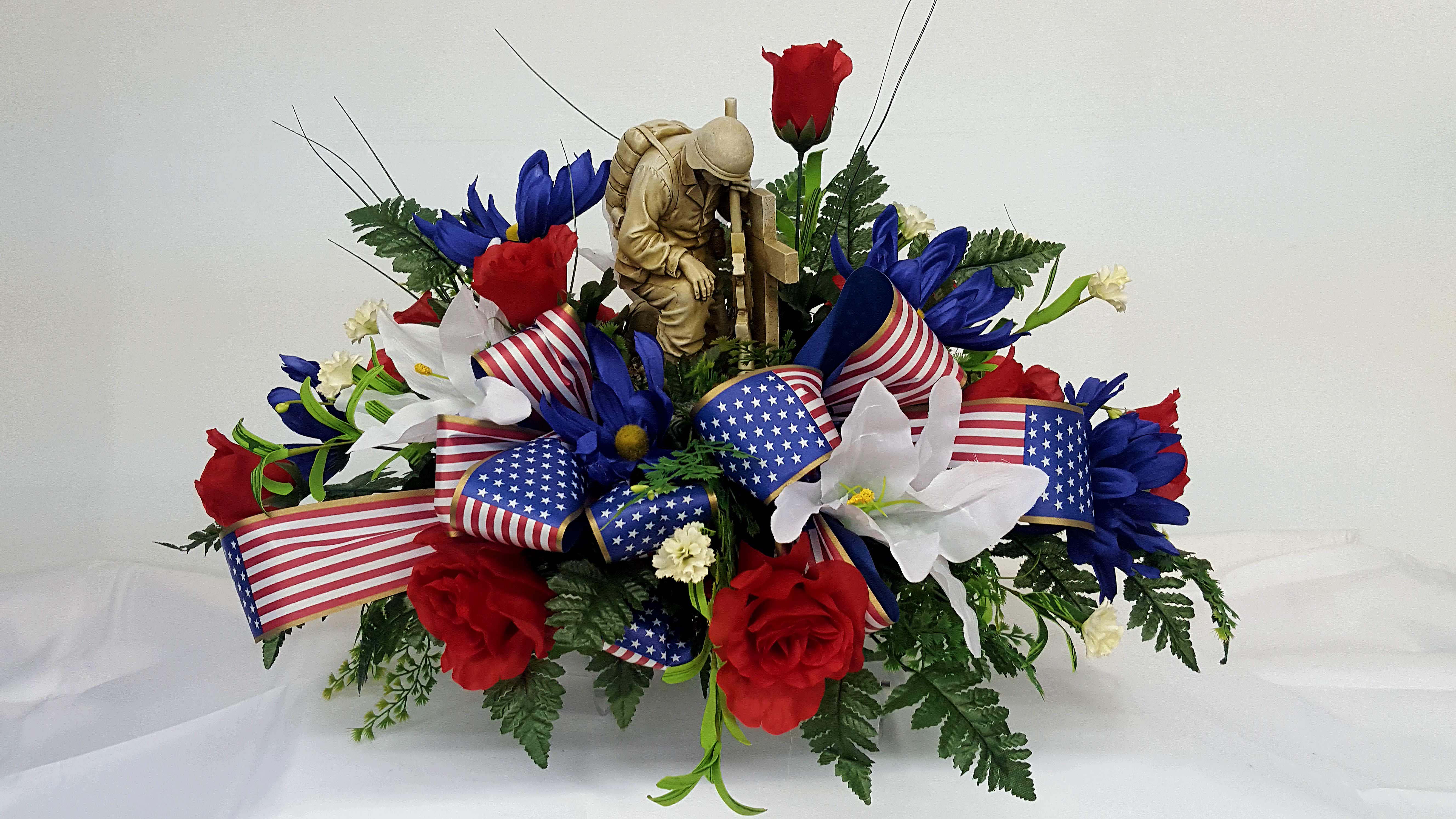 Red, white, and blue floral arrangement with patriotic ribbon and a soldier figurine