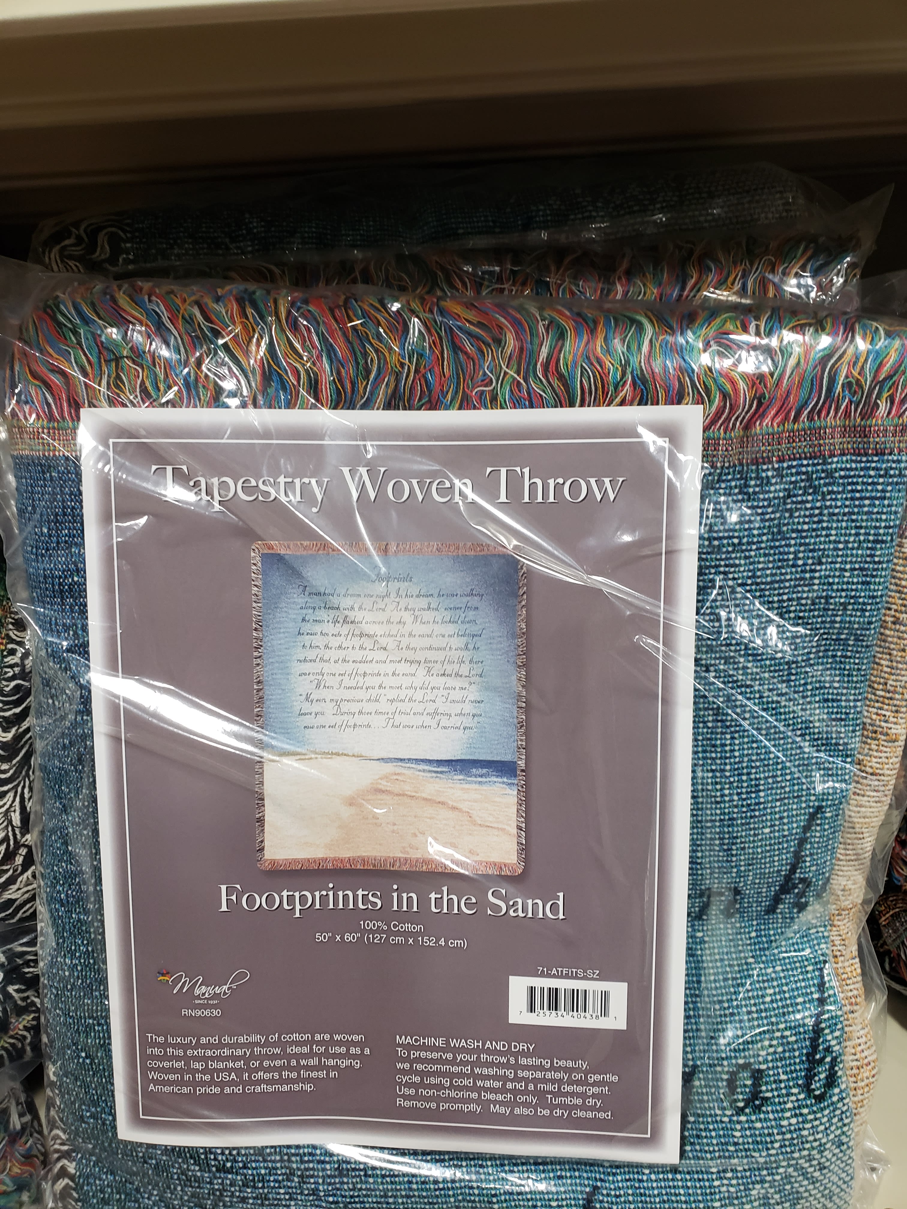 Packaged woven throw blanket with multicolored fringe and a beach scene label