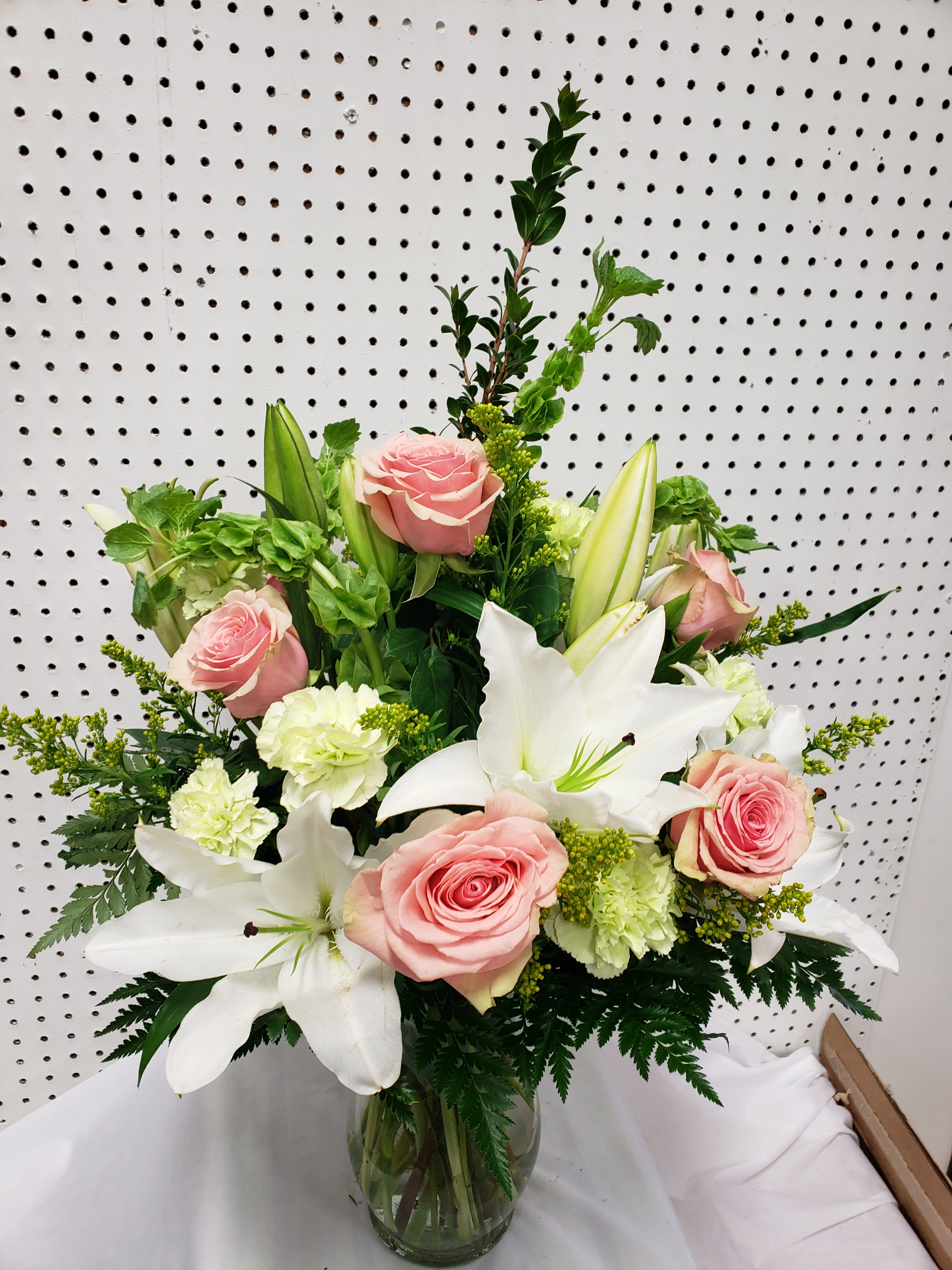 Pink roses and white lilies in a glass vase with green accents
