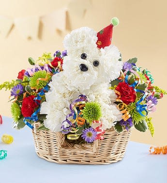 White teddy bear in a basket surrounded by colorful flowers and ribbons