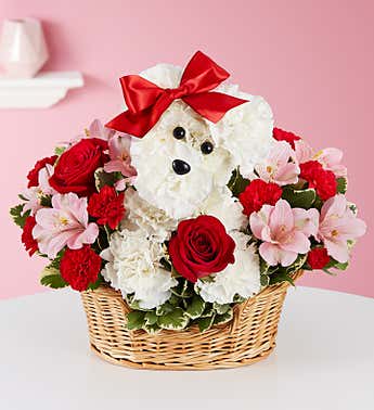 White teddy bear with a red bow in a basket of red and pink flowers