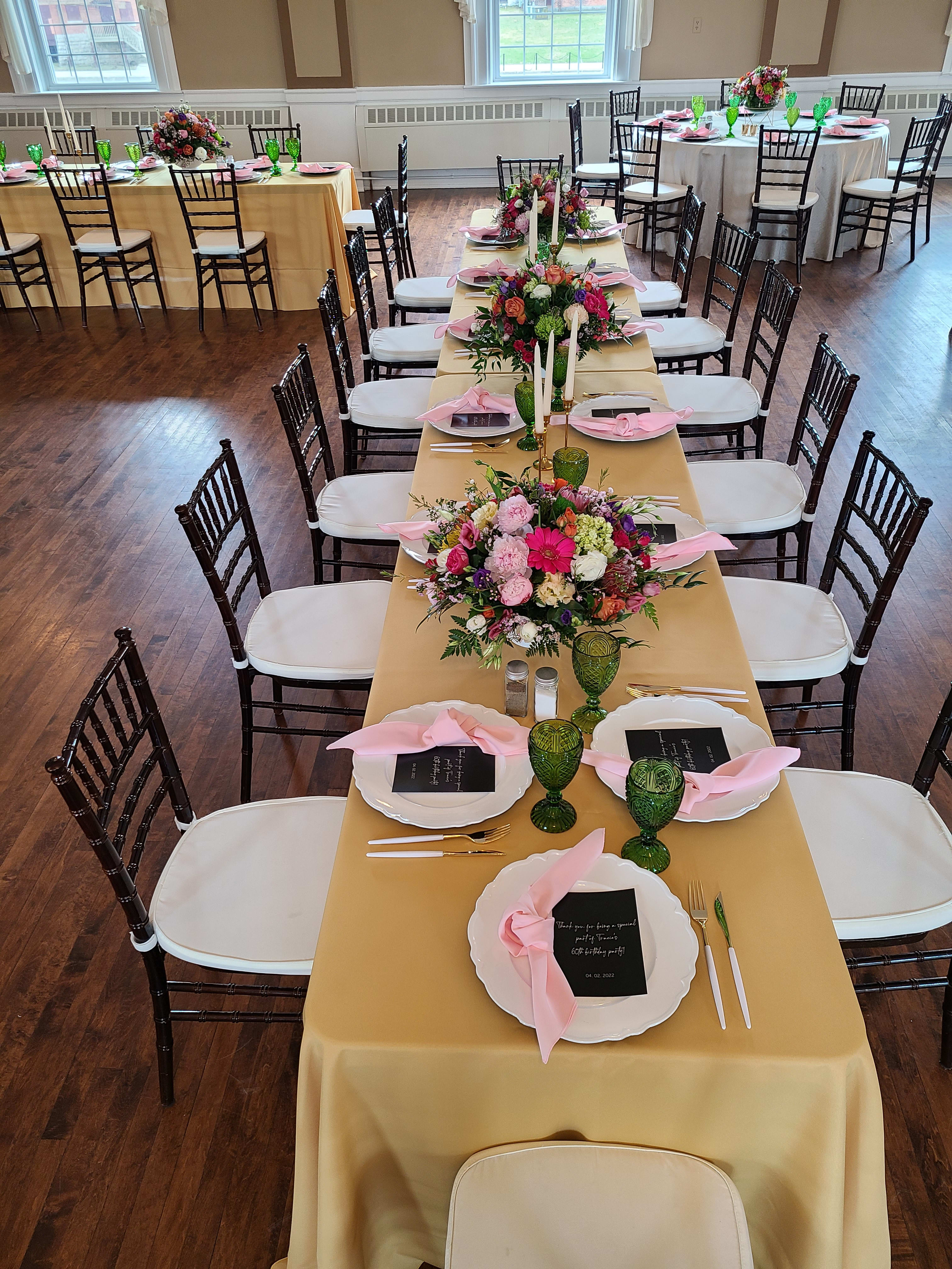 Long banquet table with low mixed pink and white floral centerpieces, white tapers, and place settings.
