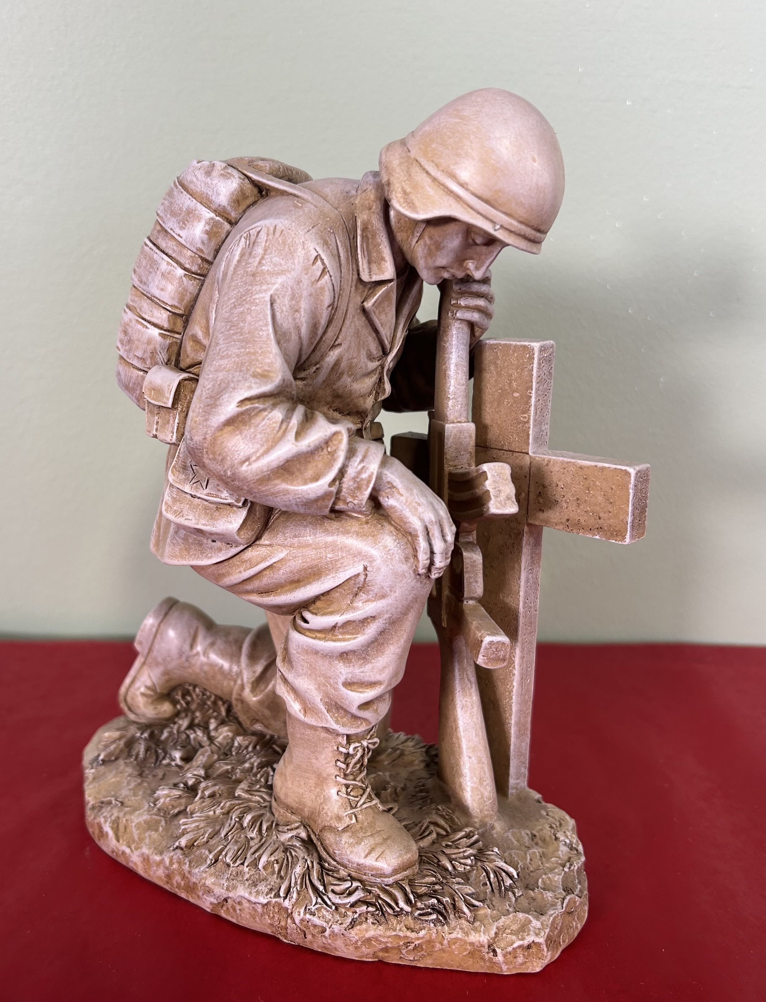 Stone soldier kneeling beside a cross memorial statue